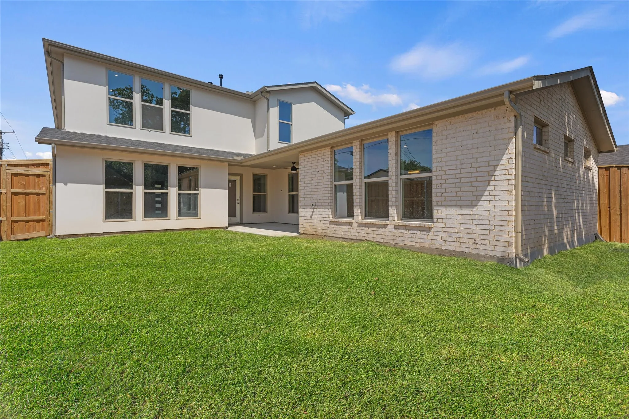 Expansive backyard featuring a manicured lawn, a light brick exterior, and a stucco finish