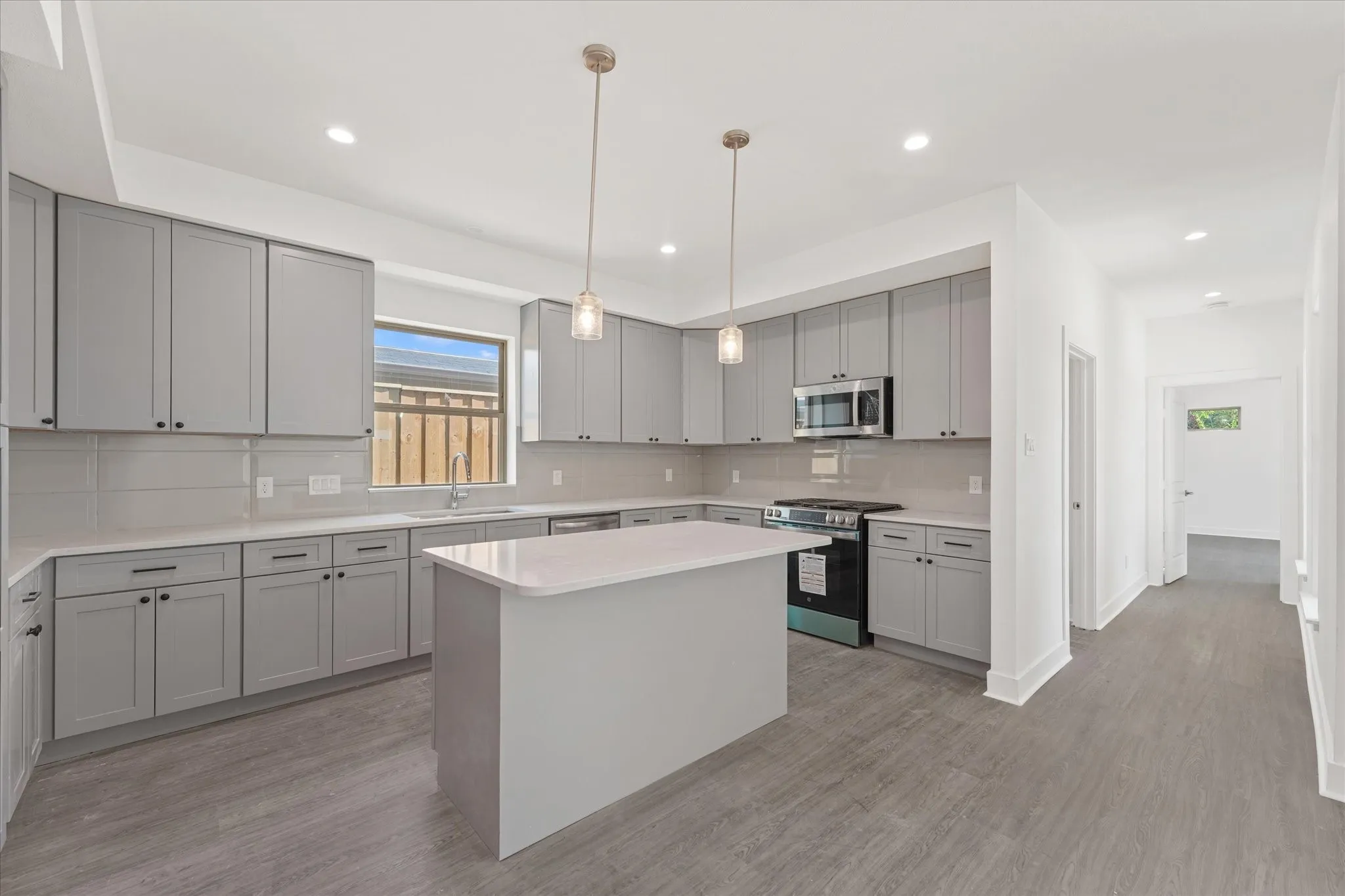 Contemporary kitchen featuring gray shaker-style cabinetry, white countertops, stainless steel appliances, a center island, and wood-finish flooring