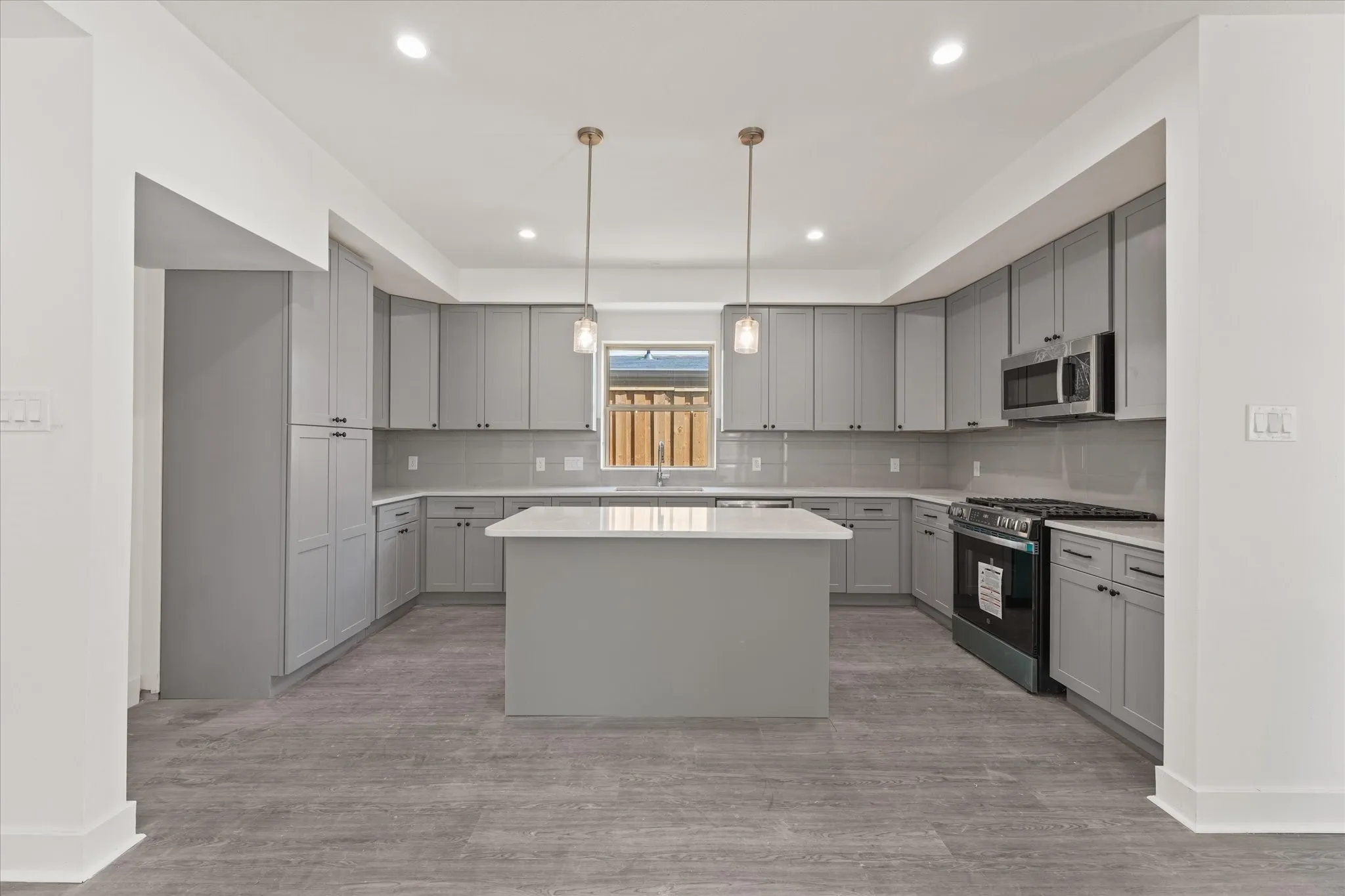 Spacious kitchen featuring gray cabinetry, a central island, stainless steel appliances, pendant lighting, and wood-finish flooring