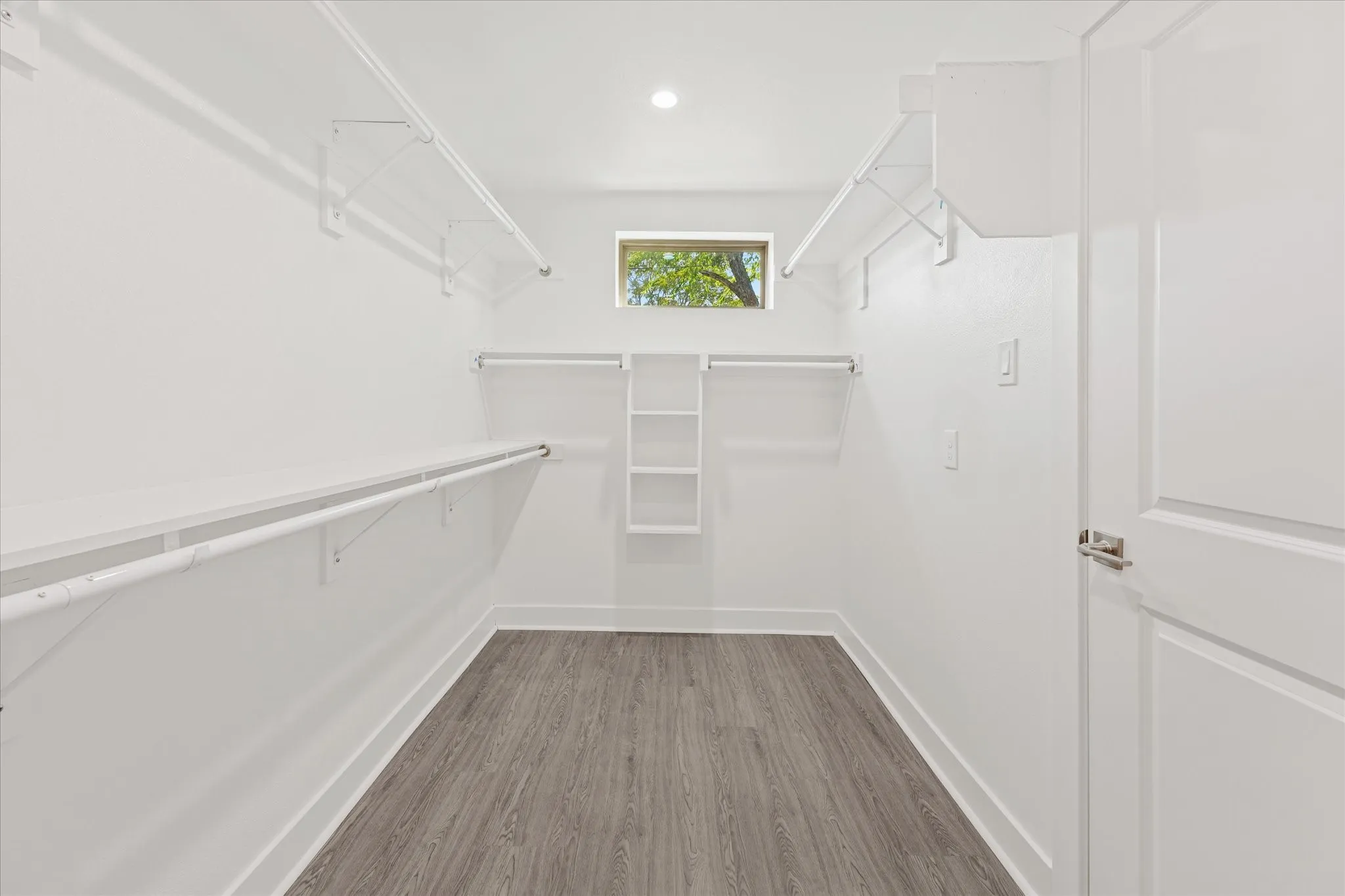 Walk-in closet featuring wood-finish flooring, built-in shelving, hanging rods, and a window for natural illumination