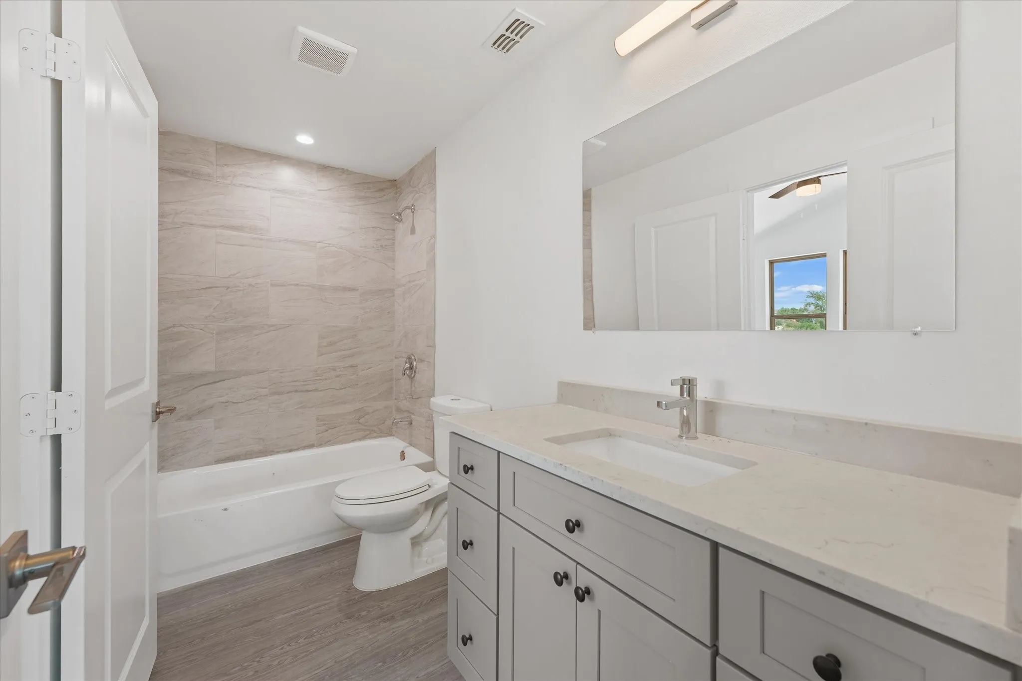 Wood-finish flooring throughout, modern entry door with frosted glass panels, recessed ceiling lighting, and a wood handrail