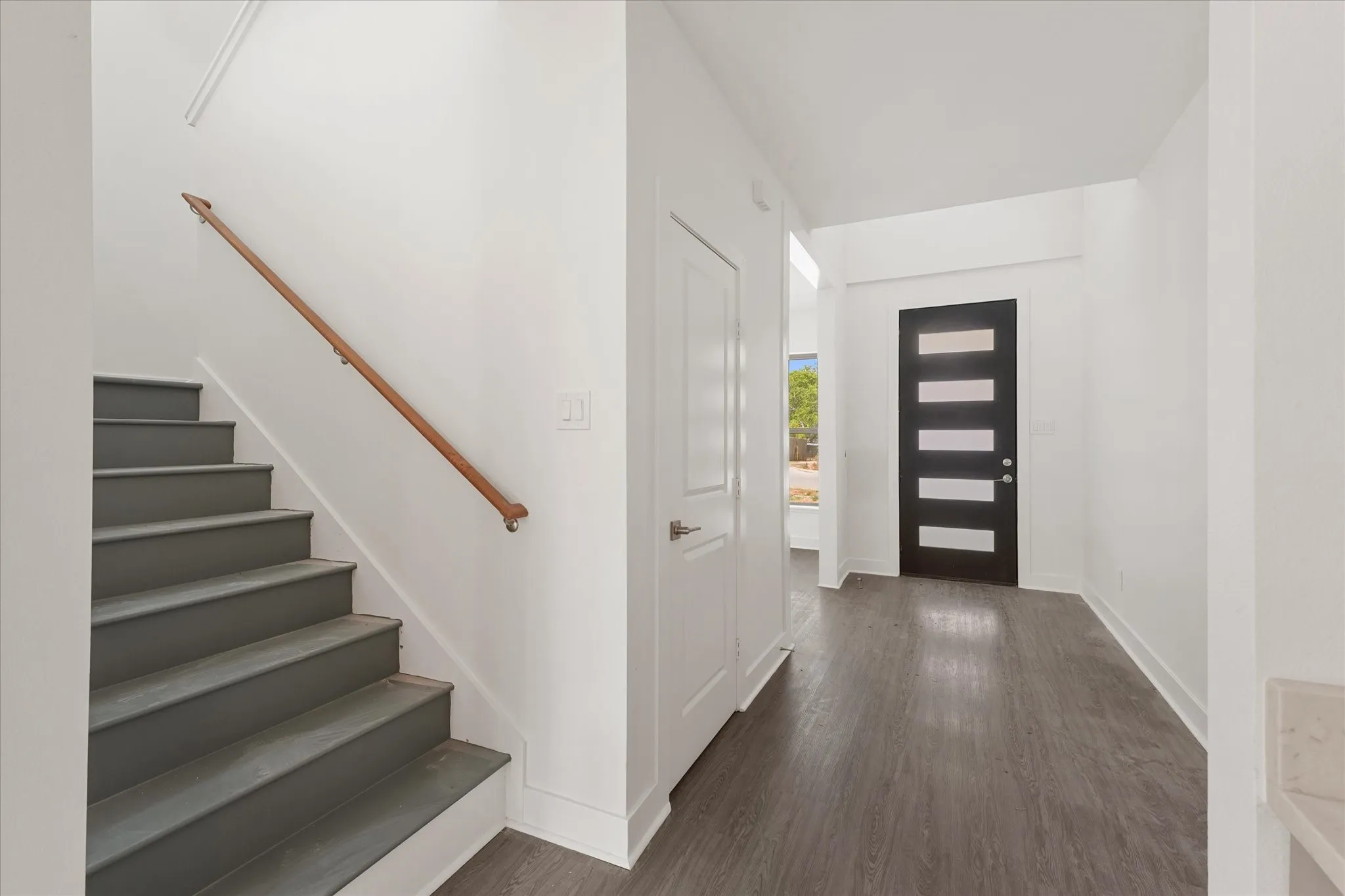 Entryway featuring wood-finish flooring, white walls, a contemporary dark entry door with horizontal lites, and a staircase with a wood handrail
