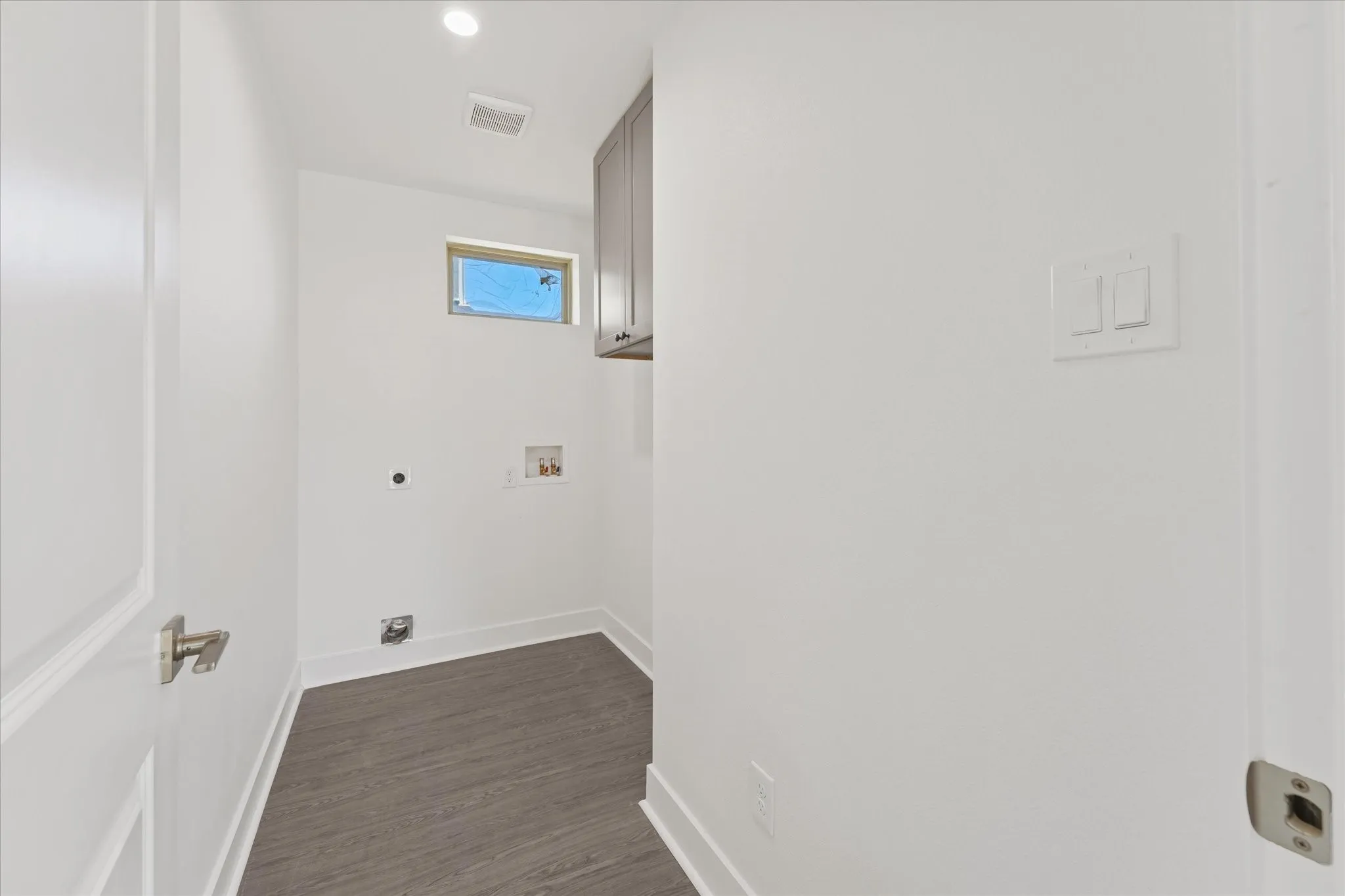 Laundry area featuring wood-finish flooring, overhead cabinetry, recessed lighting, and a transom window