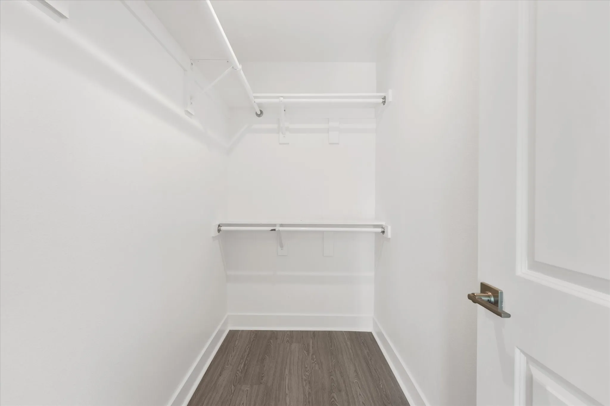 Walk-in closet featuring wood-finish flooring, white walls, and built-in shelving with hanging rods
