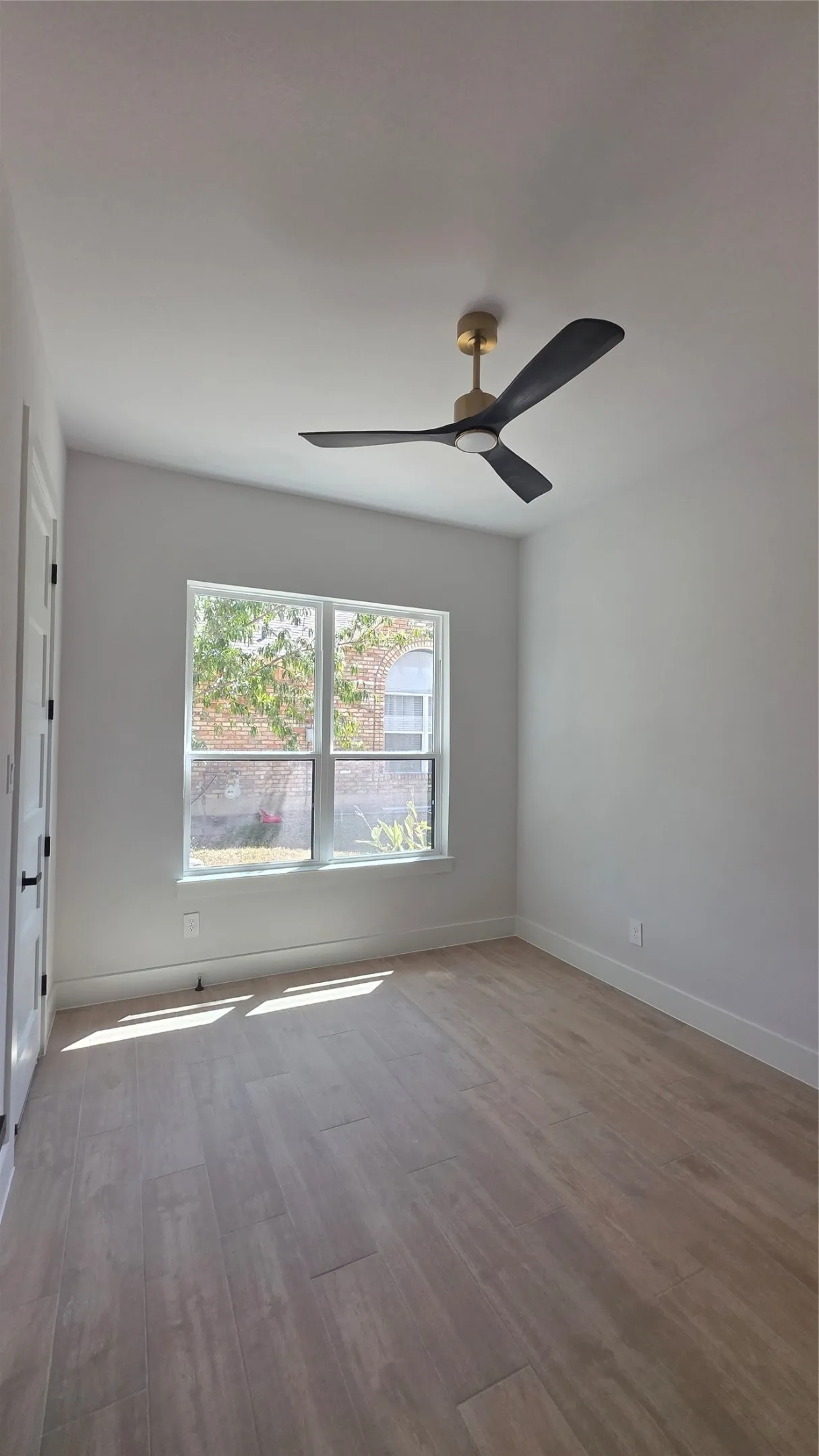 Wood-finish flooring, contemporary ceiling fan with integrated lighting, and a large window providing natural illumination