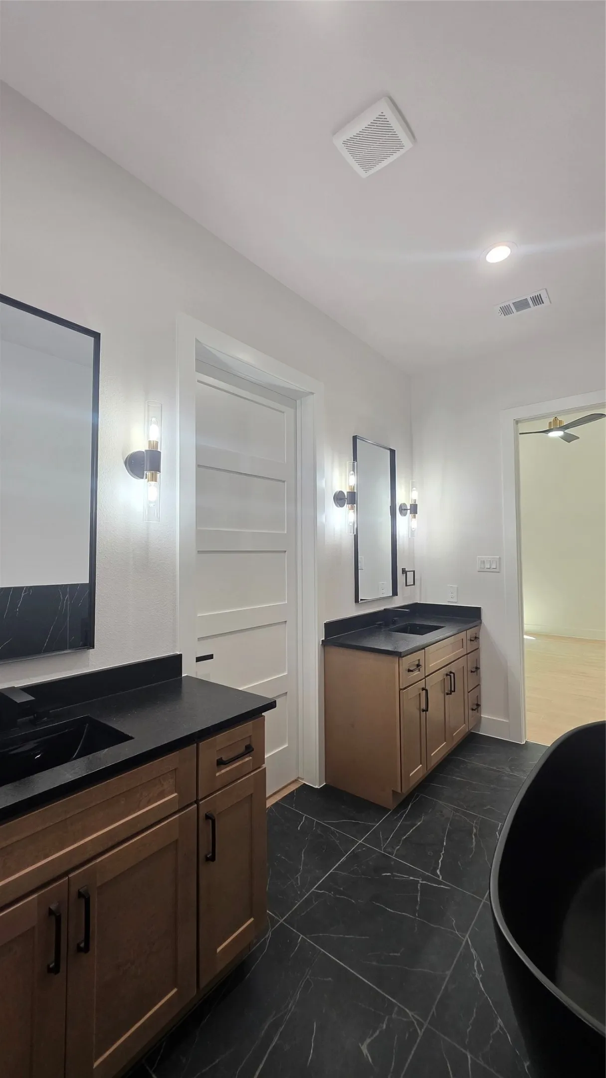 Dual wood-finish vanities with black countertops and integrated sinks