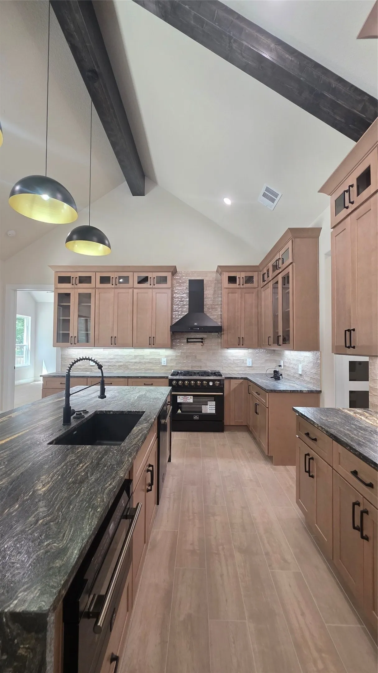 Vented vaulted ceiling with exposed beams, pendant lighting, extensive wood cabinetry, stone countertops, and wood-finish flooring