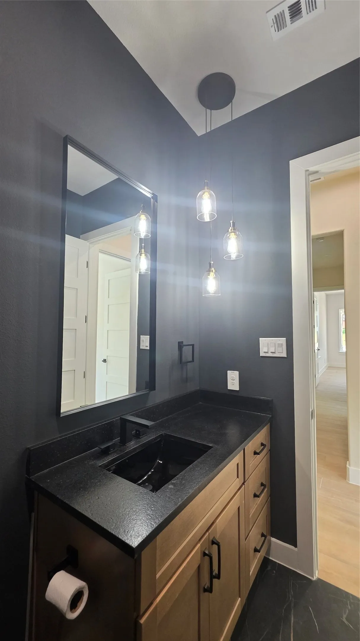 Vanity with a dark countertop and integrated sink, light wood-finish cabinetry, and matte black hardware