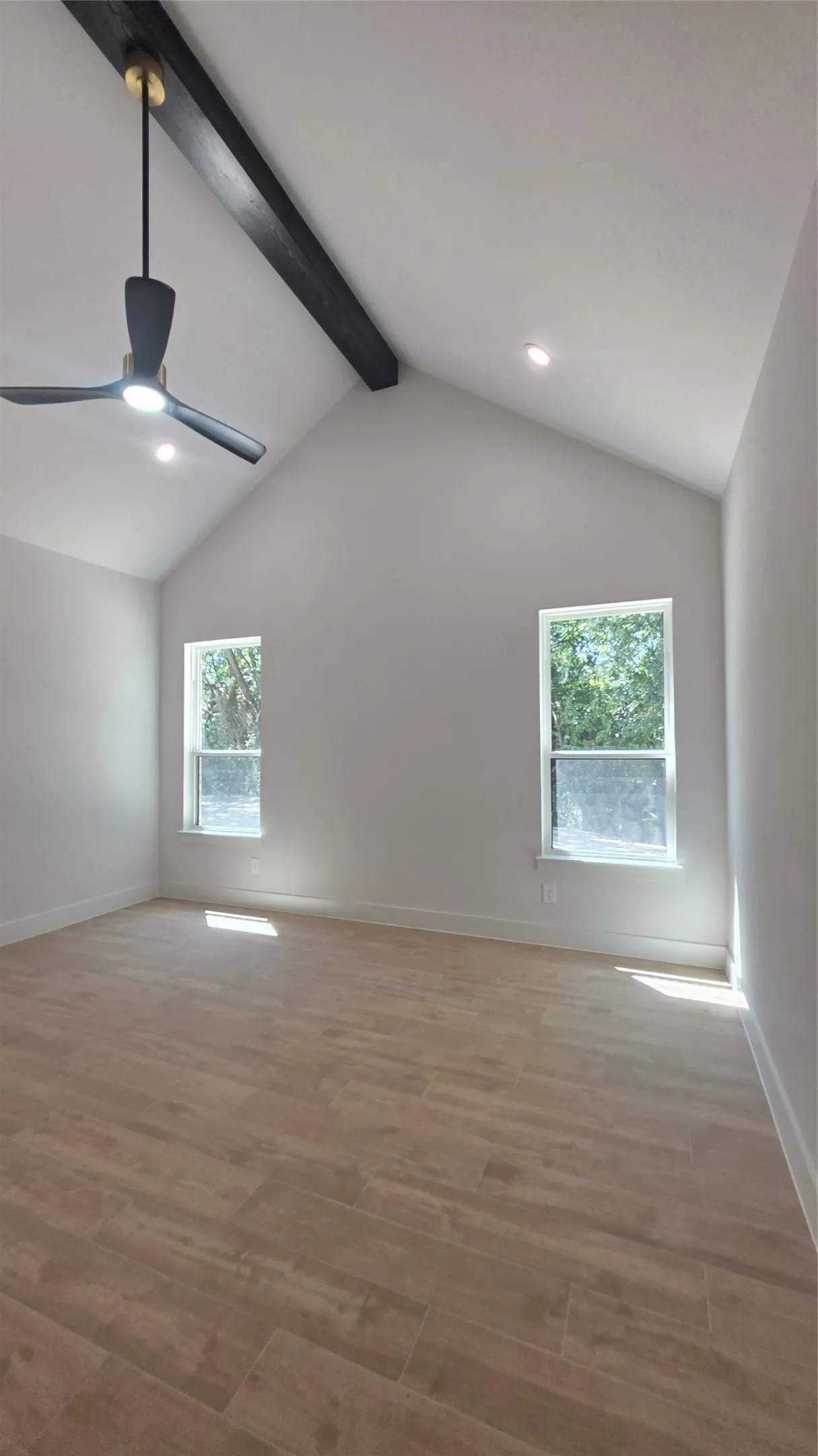 Vaulted ceiling with an exposed beam, recessed lighting, wood-finish flooring, and two windows