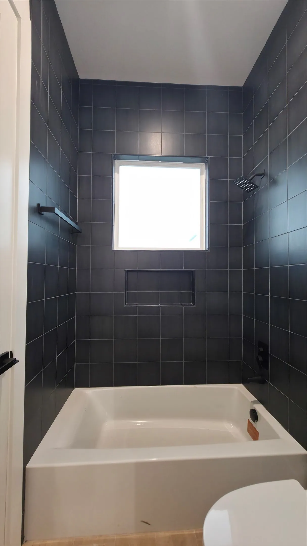 White bathtub with black tiled surround, integrated shower niche, and matte black shower fixtures