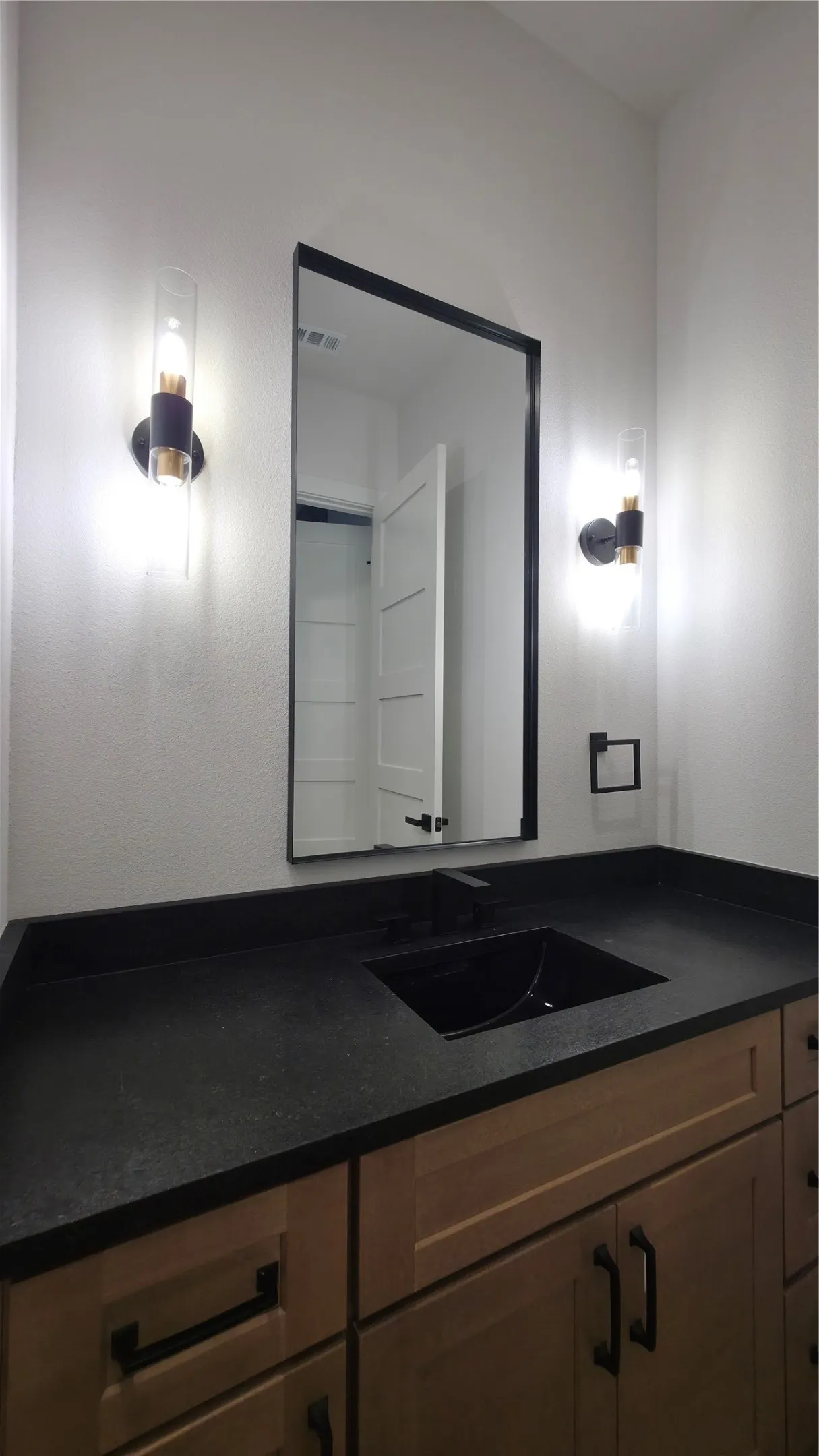 Single vanity with a dark countertop, an undermount sink with a matte black faucet, and natural wood cabinetry featuring black hardware