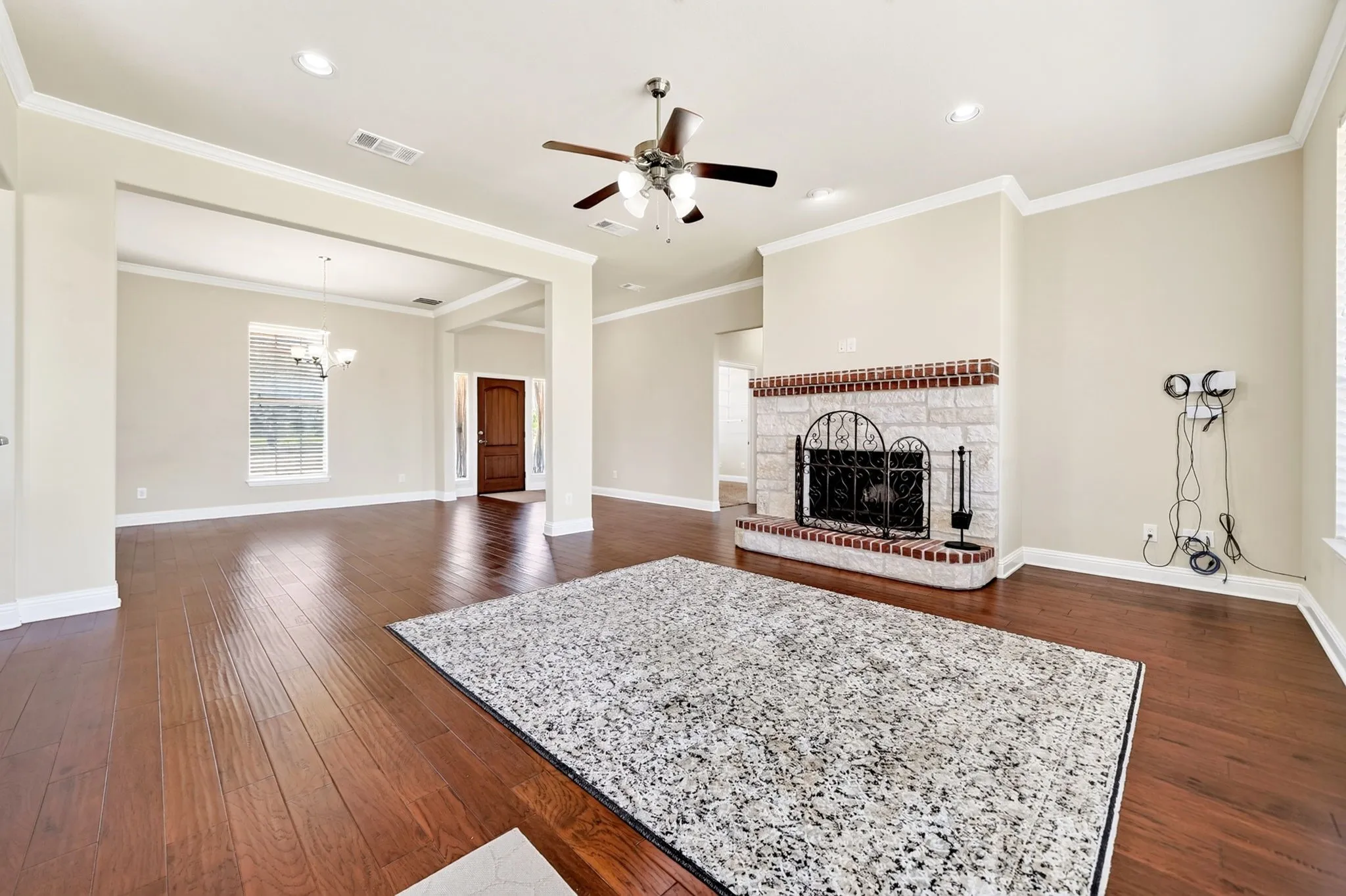Wood-finish flooring throughout, ceiling fan with integrated lighting, recessed lighting, and a stone and brick fireplace with a metal screen