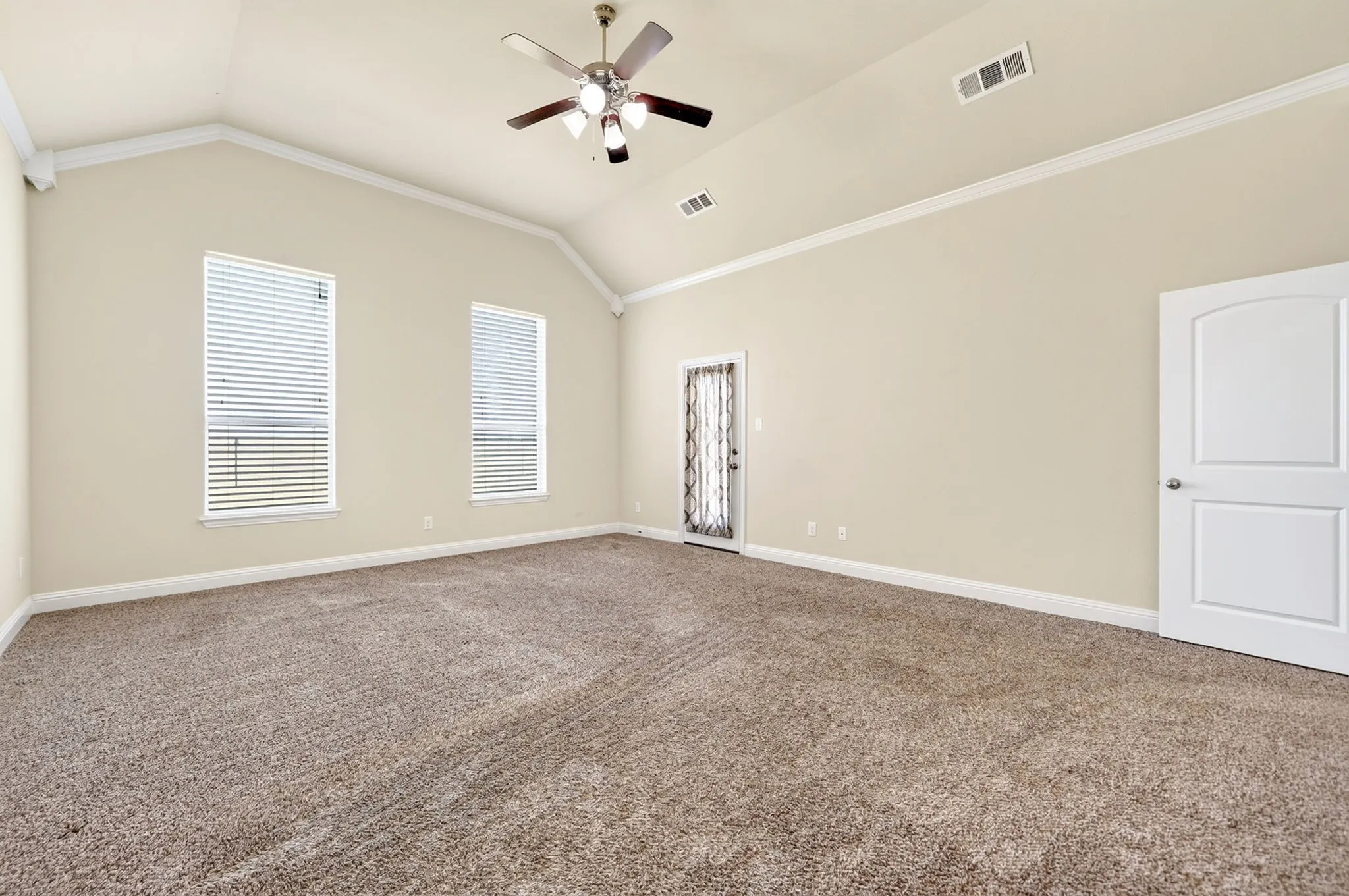 Vaulted ceiling with crown molding, ceiling fan, and two windows with blinds. private doorway to covered back porch.