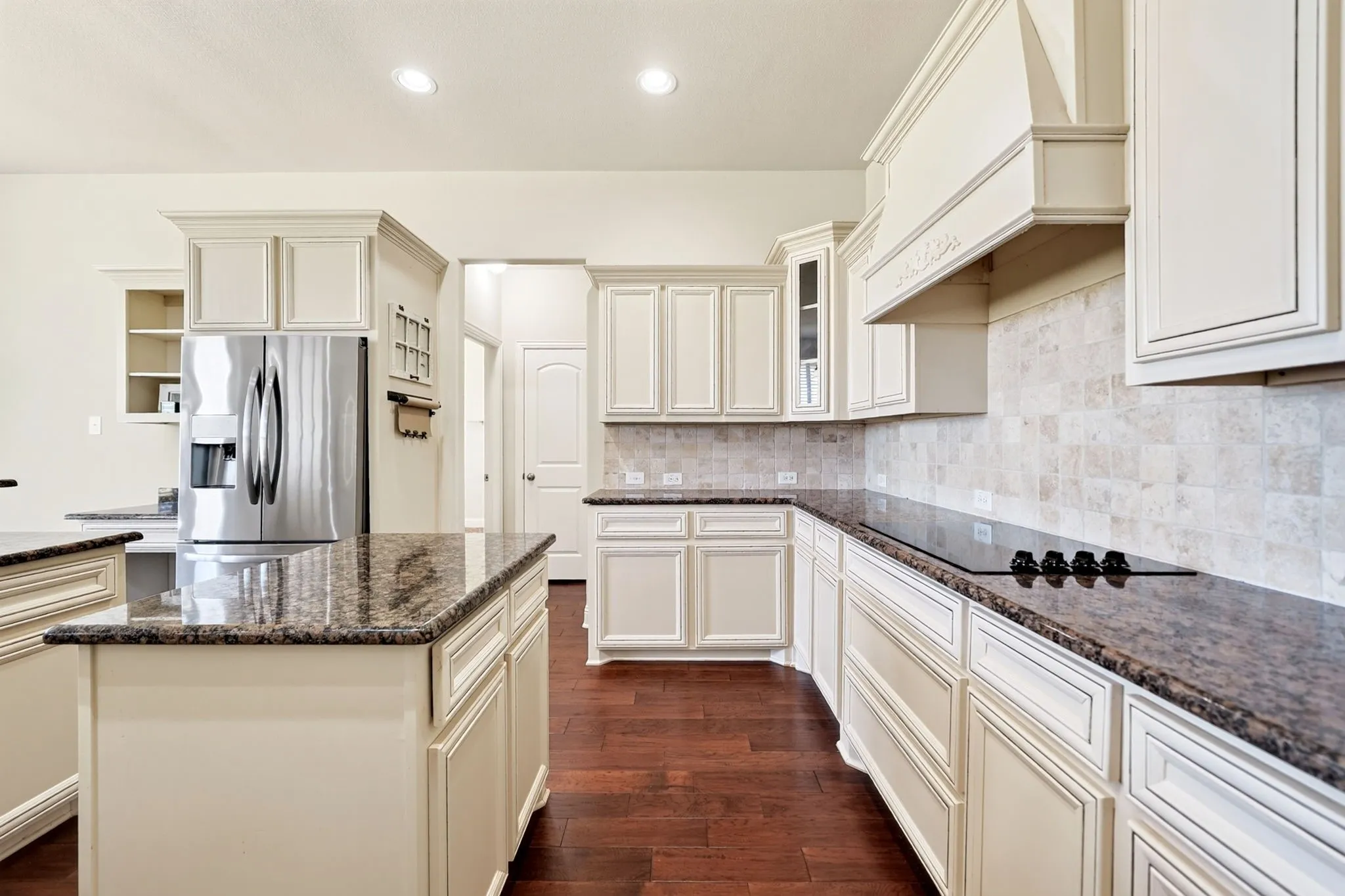 Kitchen featuring a large island, wood-finish flooring, white cabinetry, integrated cooktop, and stainless steel refrigerator
