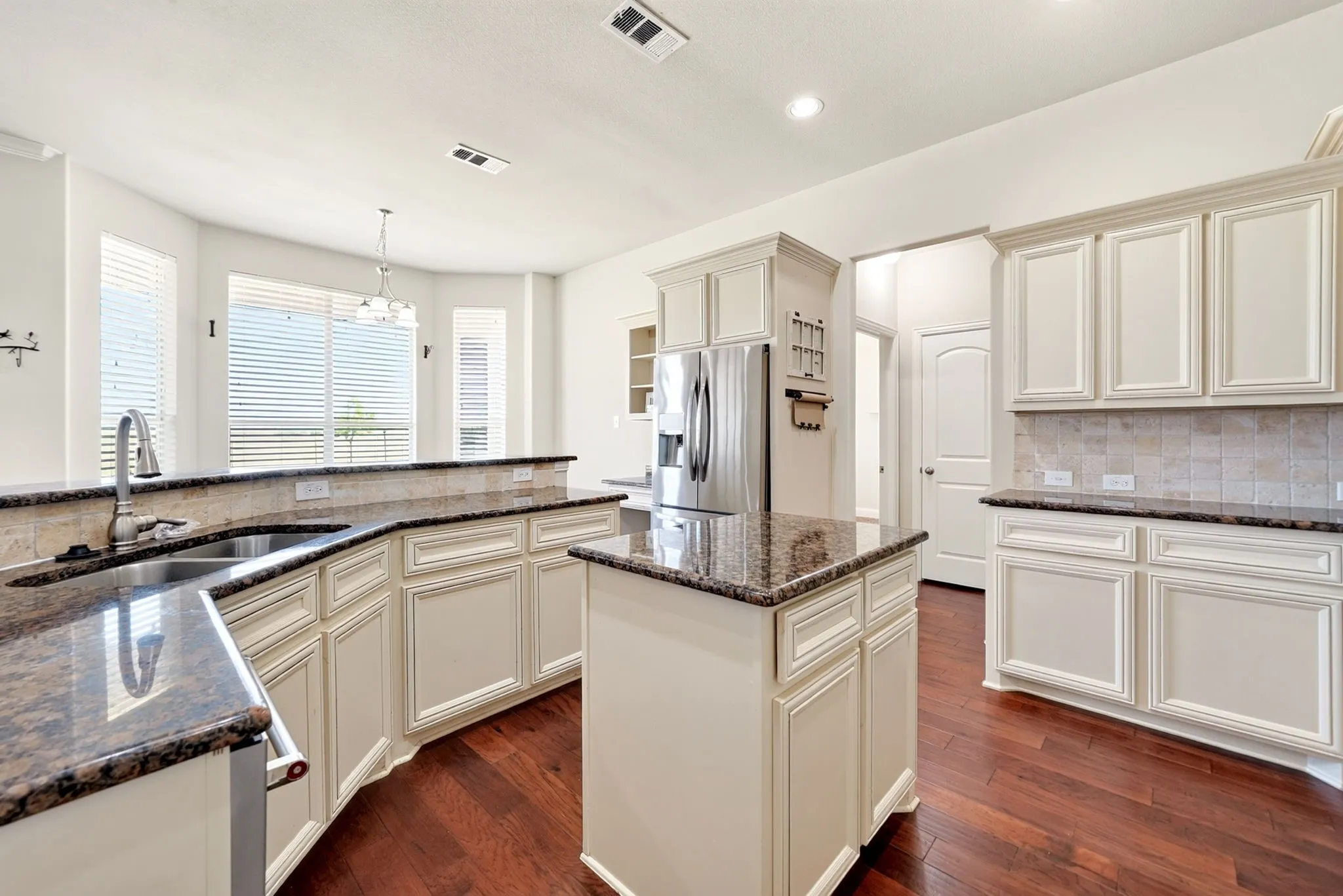 Kitchen featuring extensive cabinetry, stainless steel appliances, a kitchen island, double basin sink, and wood-finish flooring