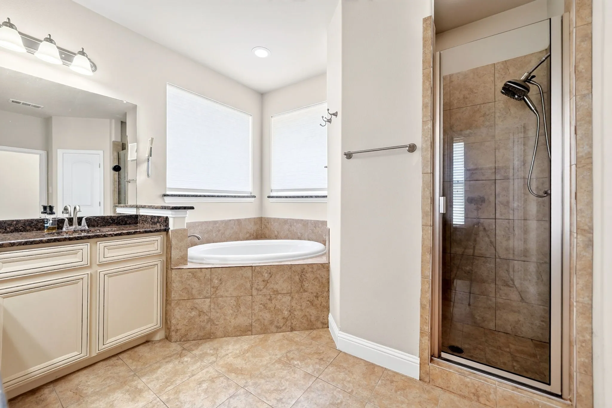 Dual vanity with a stone countertop, built-in soaking tub, and a separate glass-enclosed shower