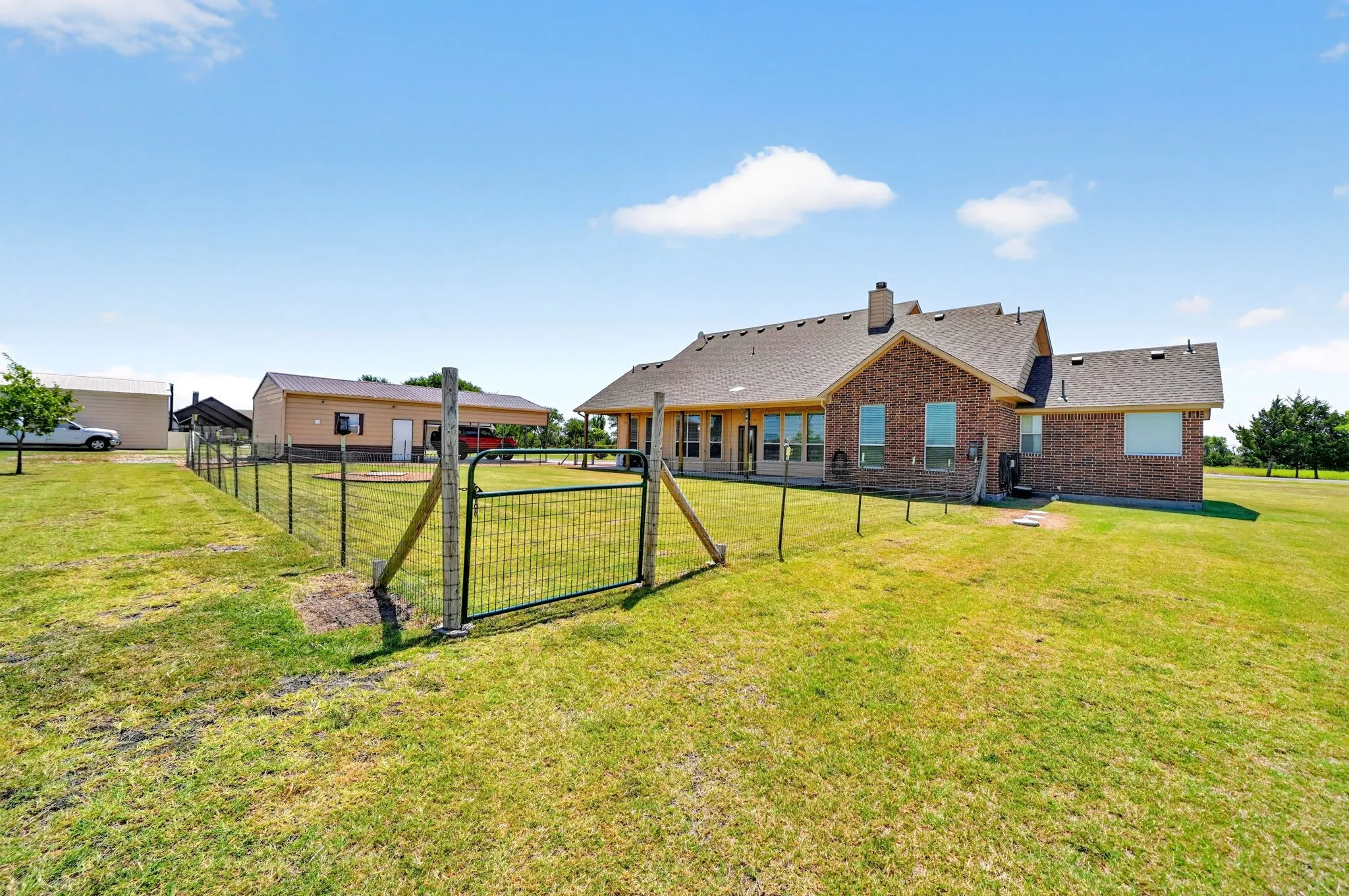 Expansive fenced yard with a brick exterior residence, multiple windows, and a detached auxiliary structure