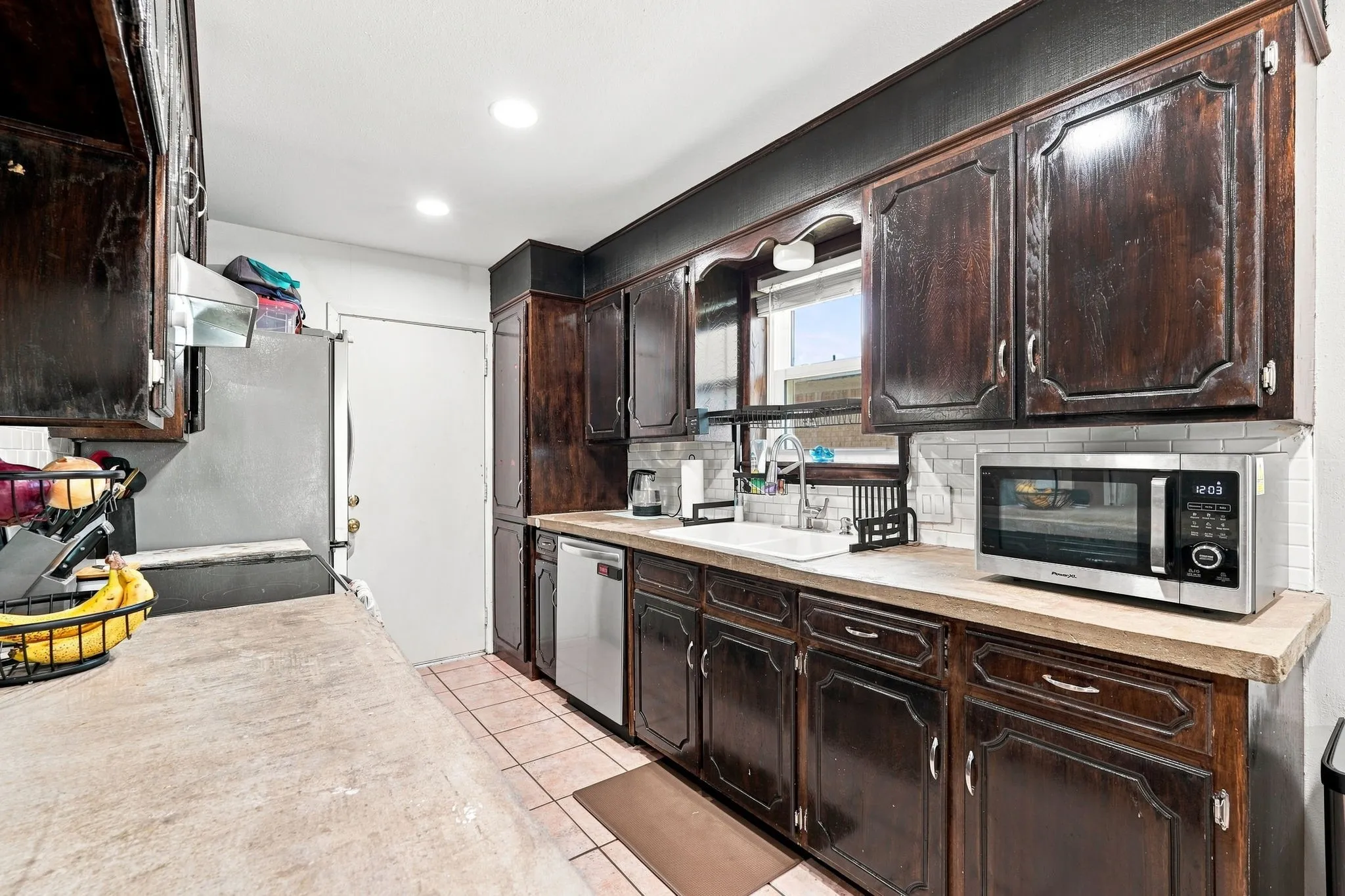 Kitchen featuring dark wood cabinetry, light-toned countertops, white subway tile backsplash, and ceramic tile flooring