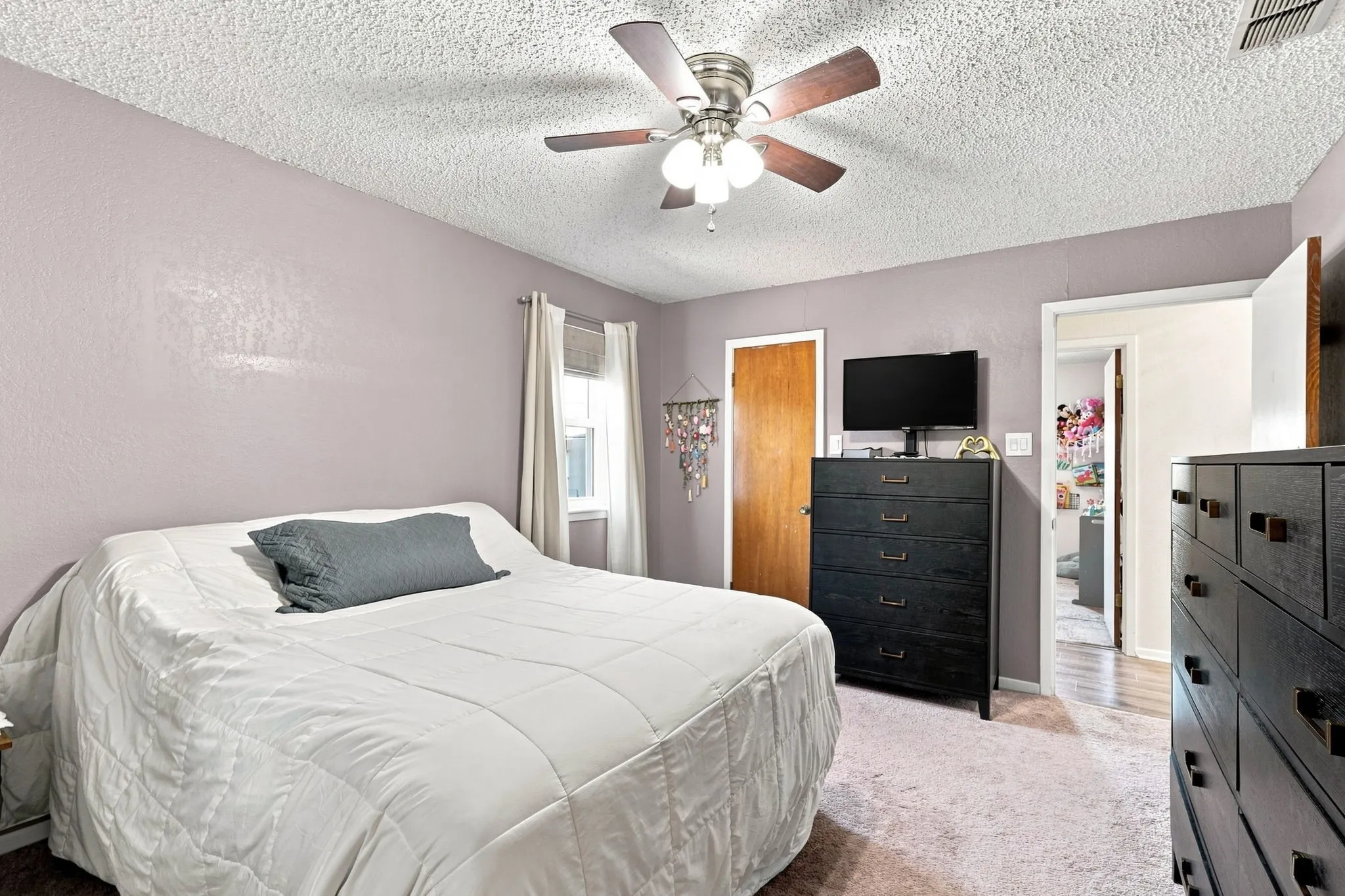 Textured ceiling with a ceiling fan, window with curtains, and wood-finish flooring