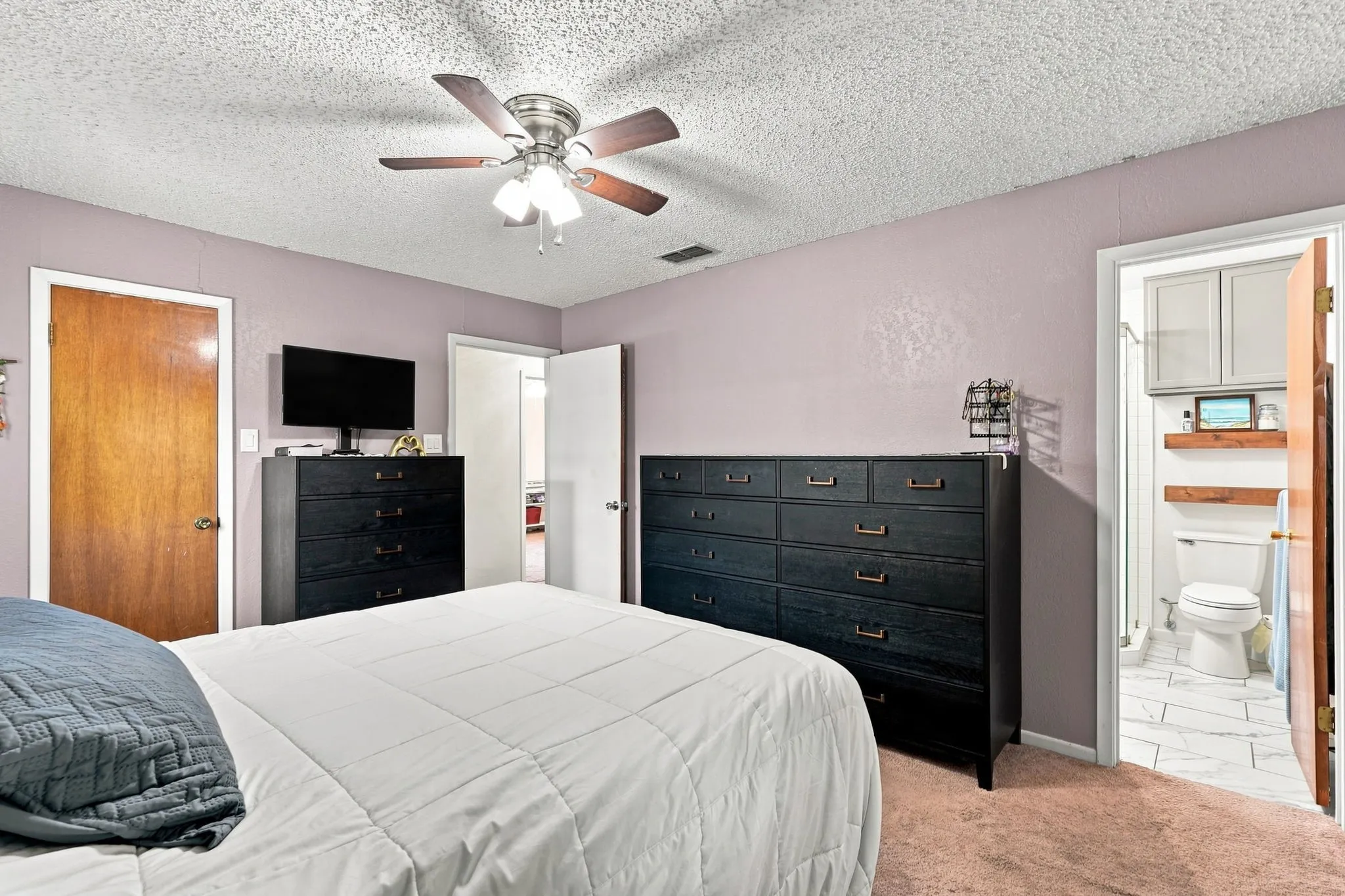 Ceiling fan with integrated lighting, wood-finish interior doors, textured ceiling, and a bathroom with tile flooring, wall-mounted shelving, and built-in cabinetry
