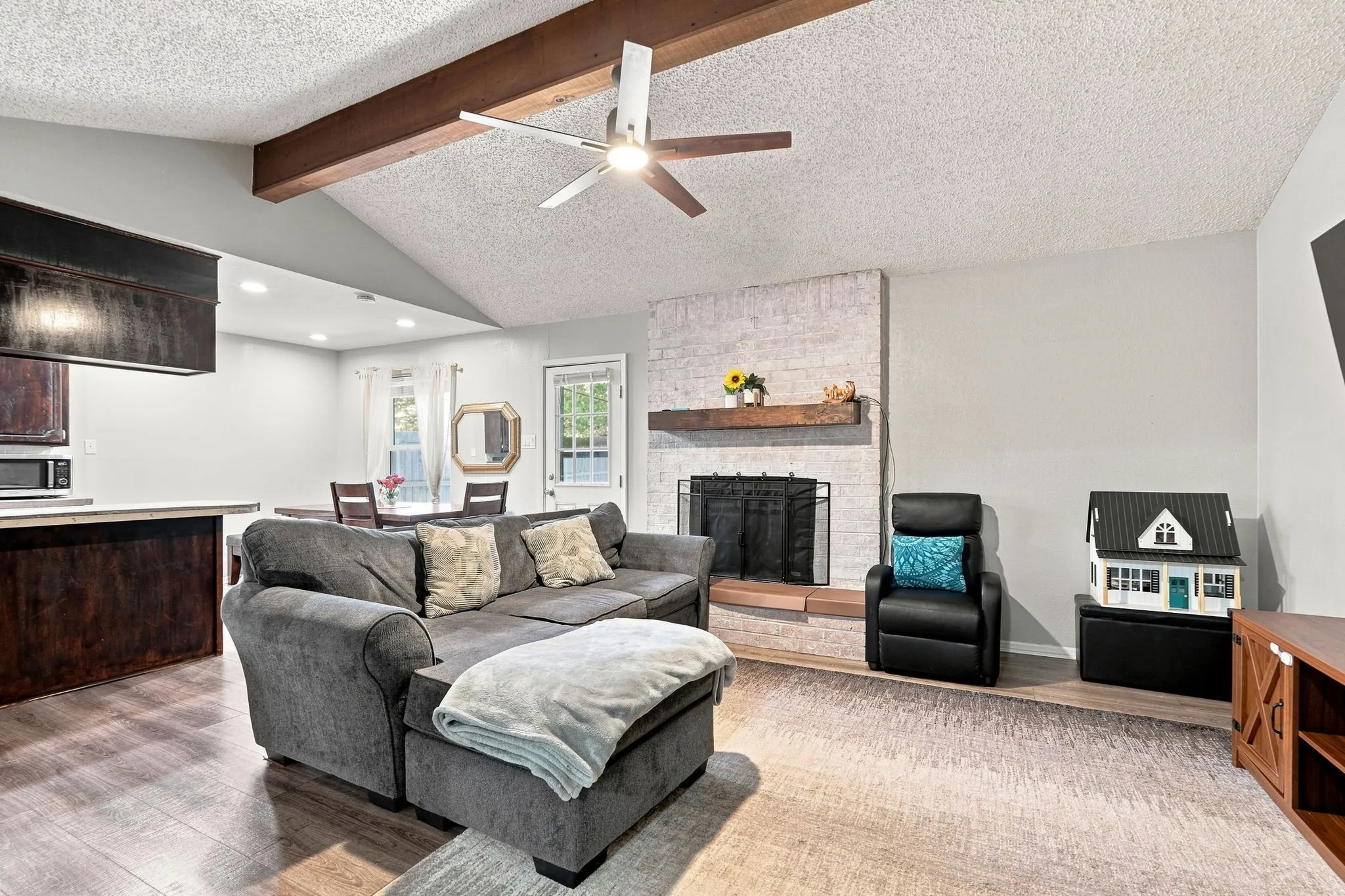 Vaulted ceiling with exposed wood beams, wood-finish flooring, recessed lighting, and a painted brick fireplace with a wood mantel
