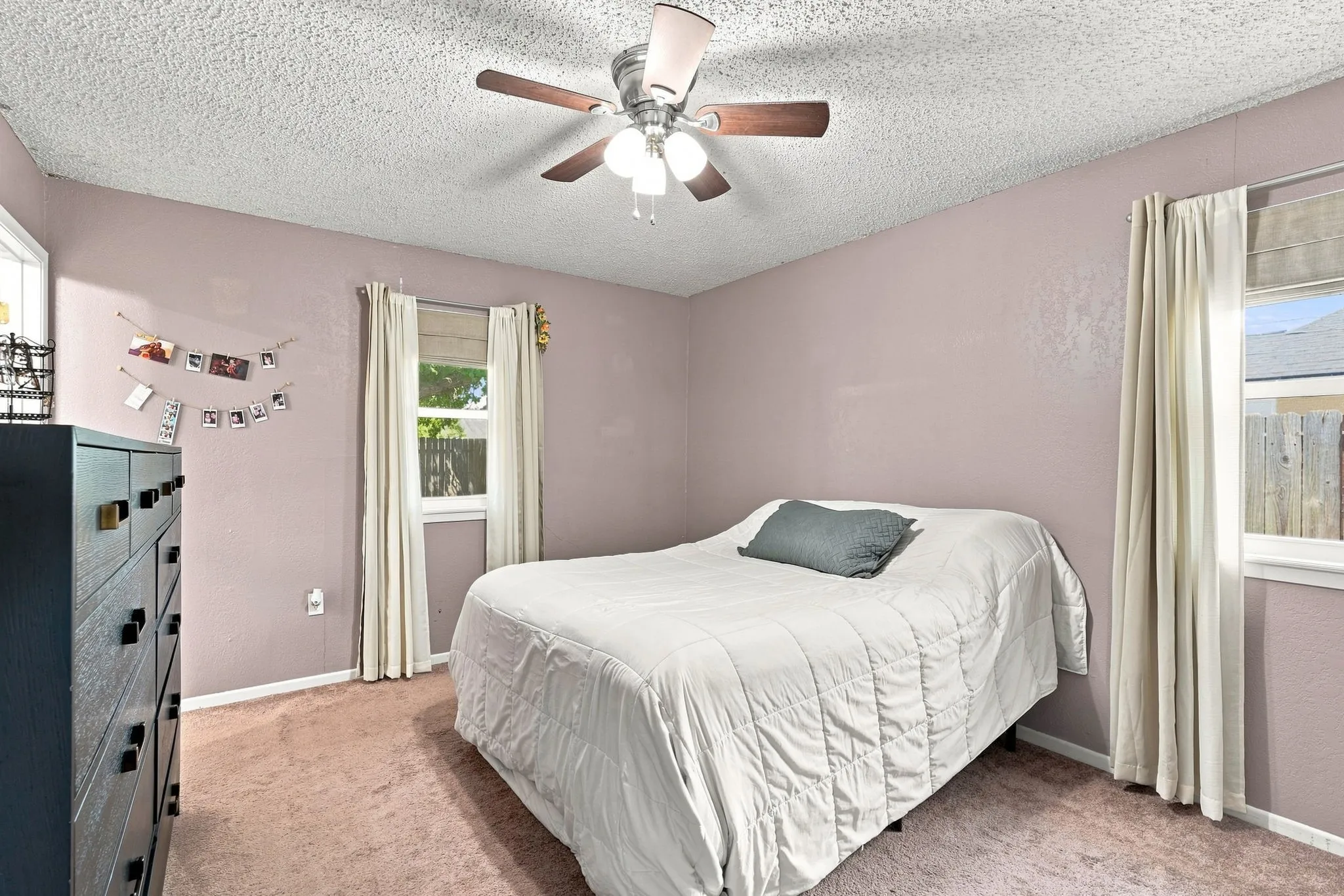 Carpeted bedroom featuring a ceiling fan with integrated lighting and two windows with natural light
