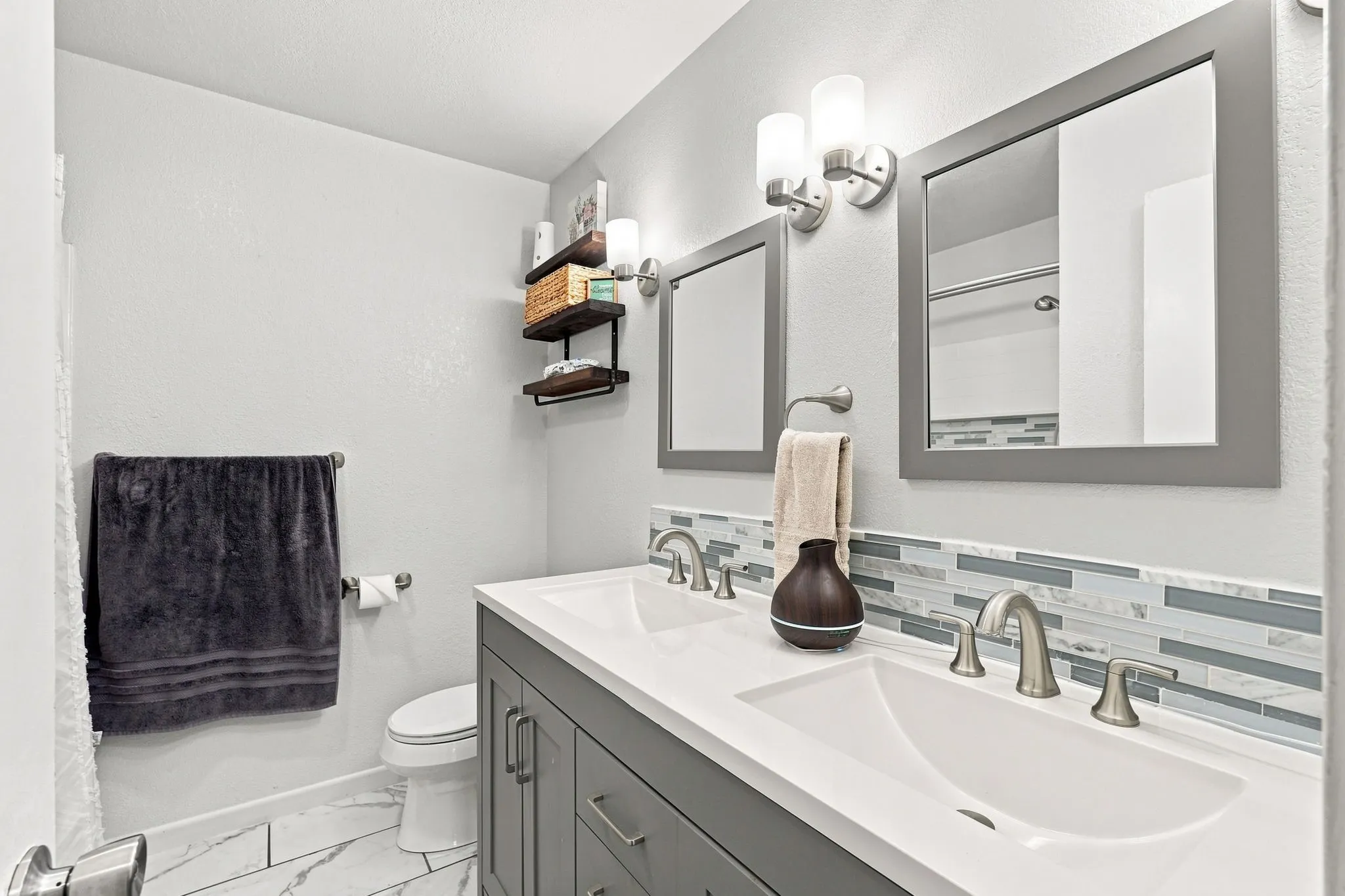 Double vanity with undermount sinks and brushed nickel faucets, white countertop, gray shaker-style cabinetry, and a mosaic tile backsplash