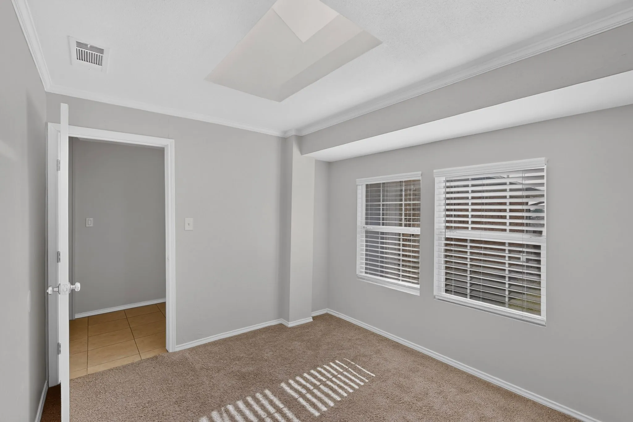 adjoining study Recessed ceiling light, crown molding, two windows with blinds, light-colored carpeting, and a doorway to a tiled space
