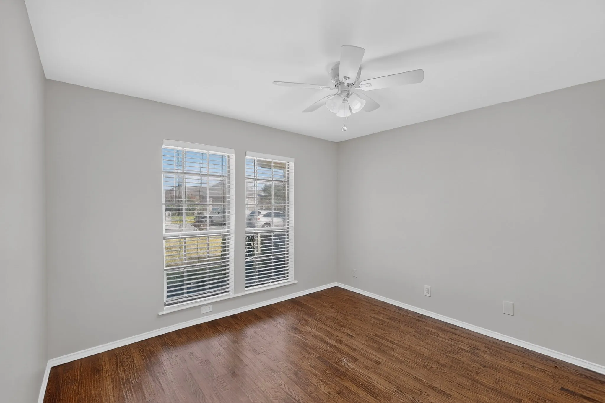 Wood-finish flooring, white walls, two windows with blinds, and an overhead ceiling fan with lighting