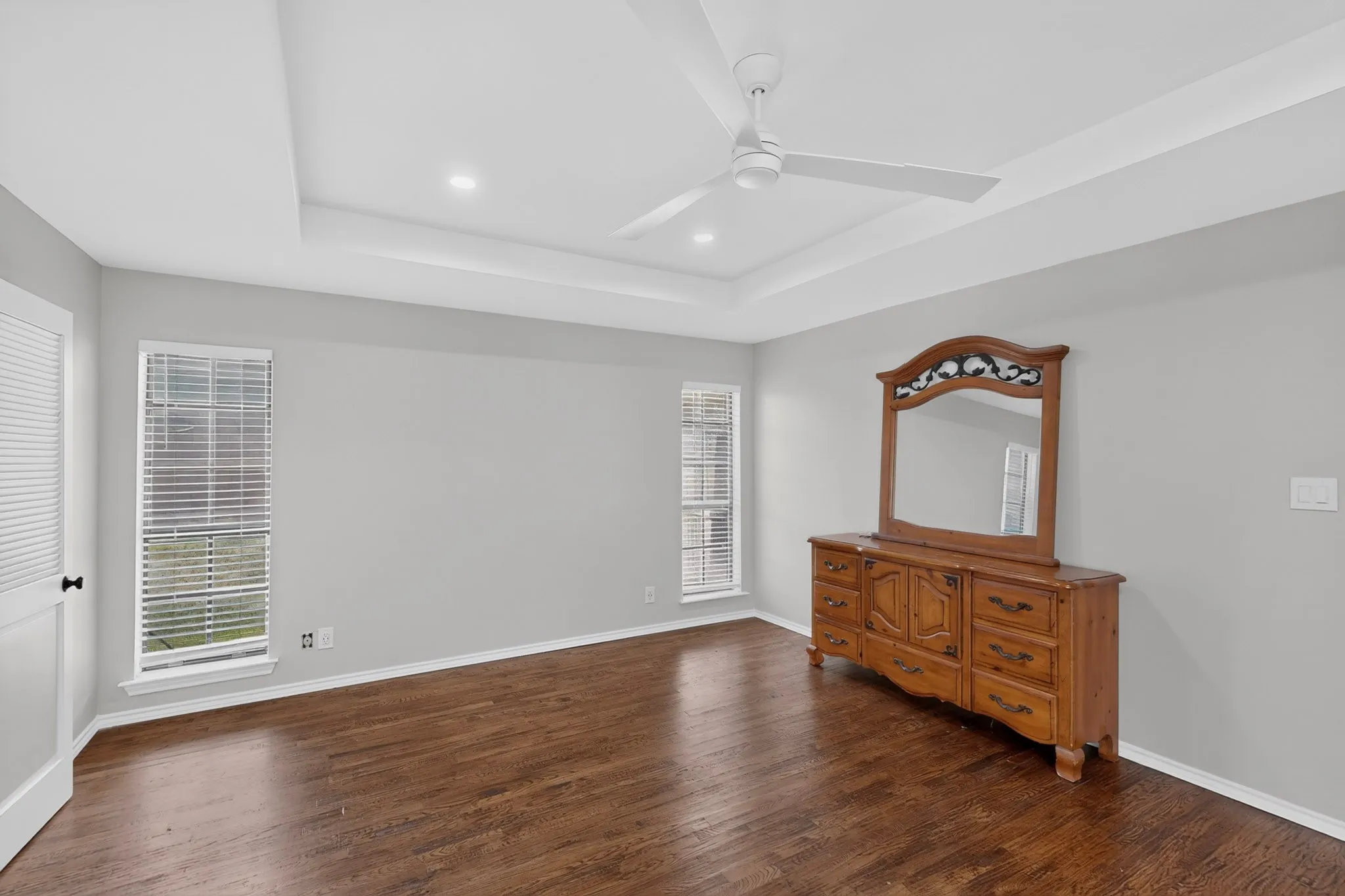 Tray ceiling with recessed lighting and a ceiling fan, complemented by wood-finish flooring