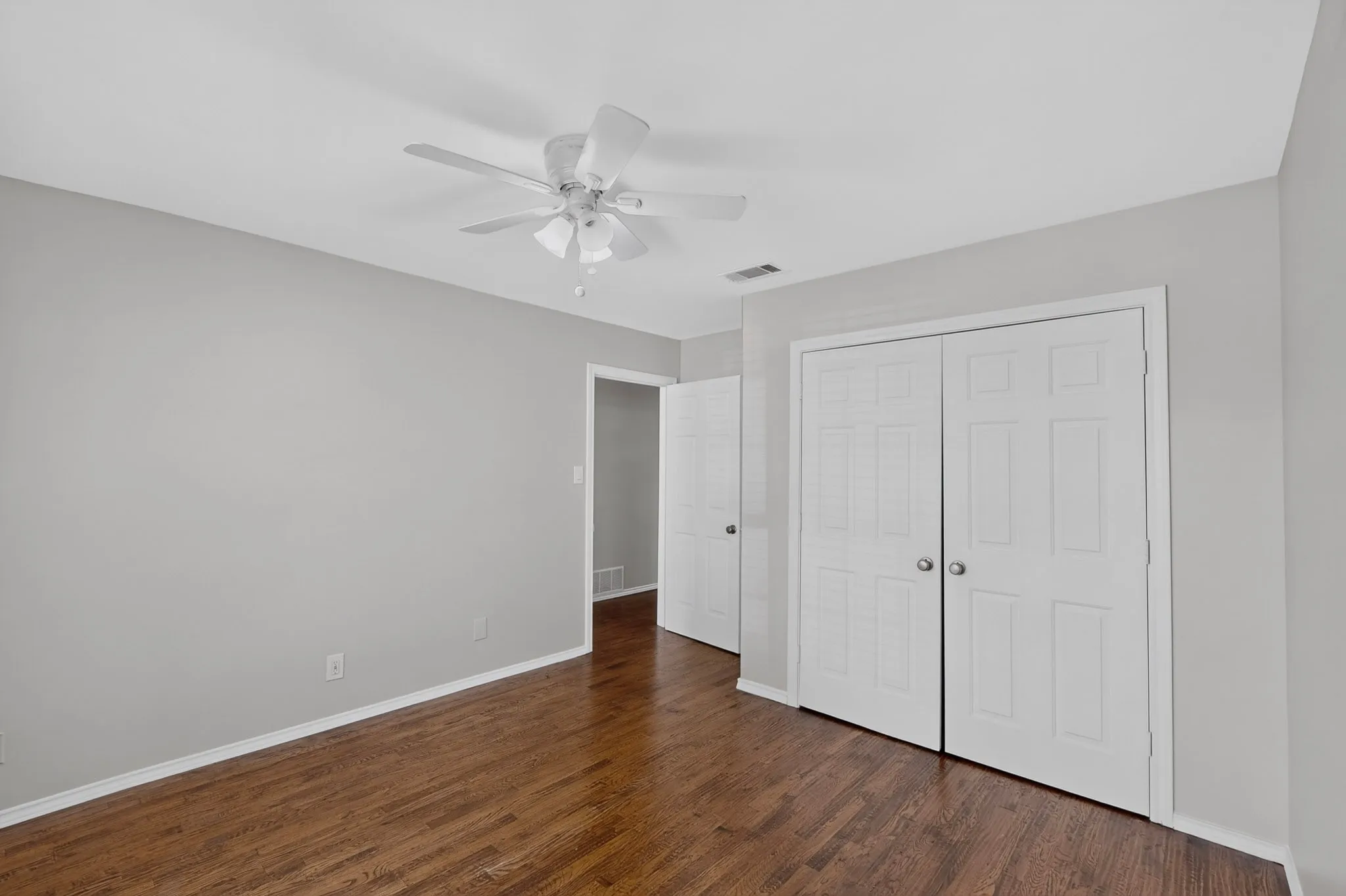 Wood-finish flooring, ceiling fan, white bi-fold closet doors, and light-toned walls