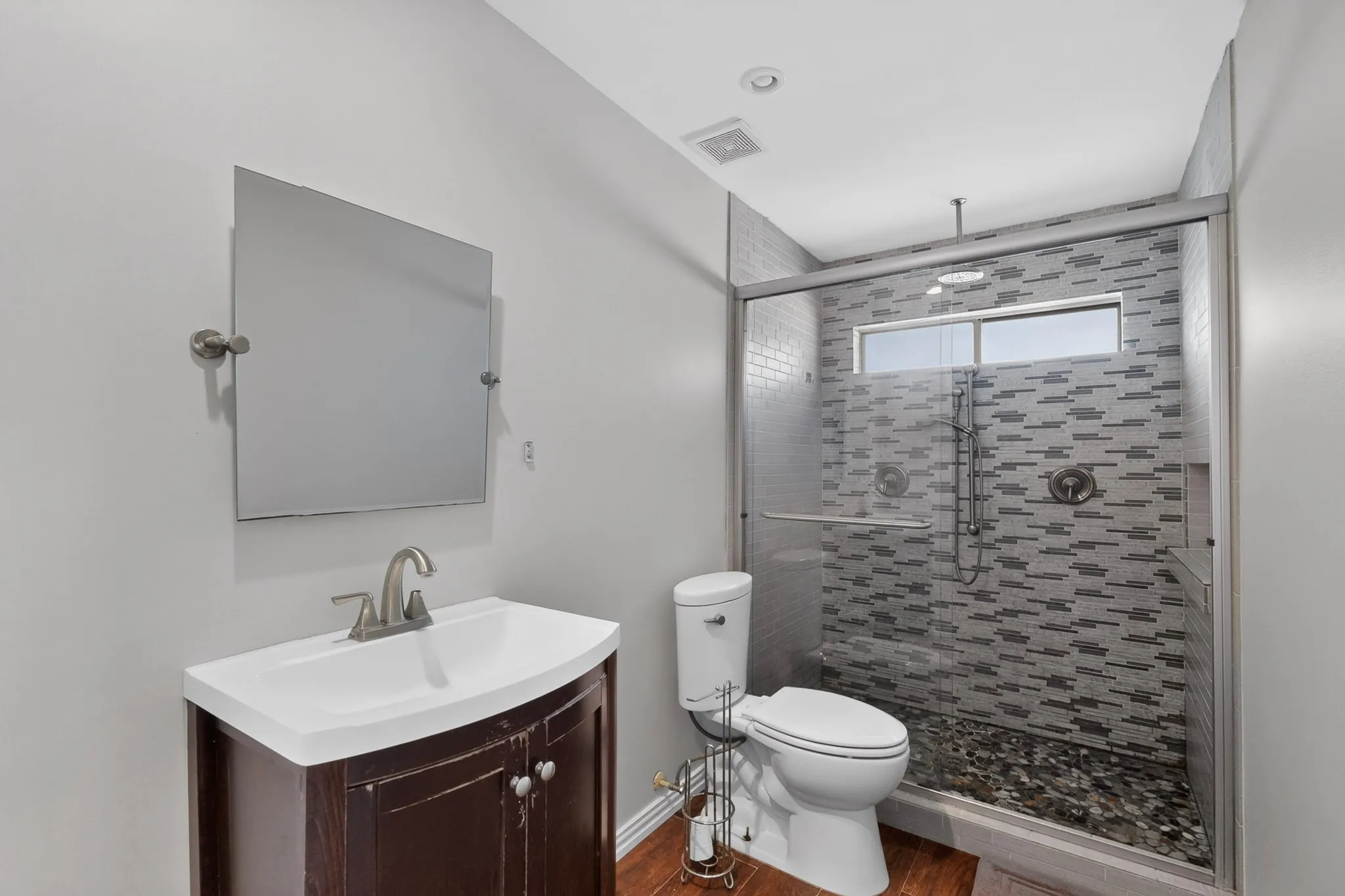 Glass-enclosed shower with mosaic tile surround and river rock base