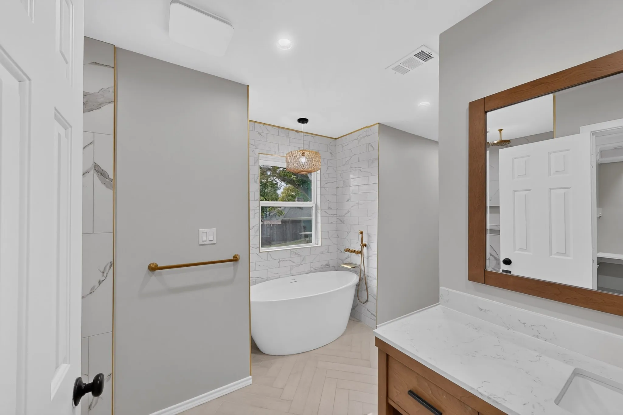 Freestanding soaking tub with gold-tone fixtures, white subway tile wall surround, and wood-finish vanity with a single basin and white countertop