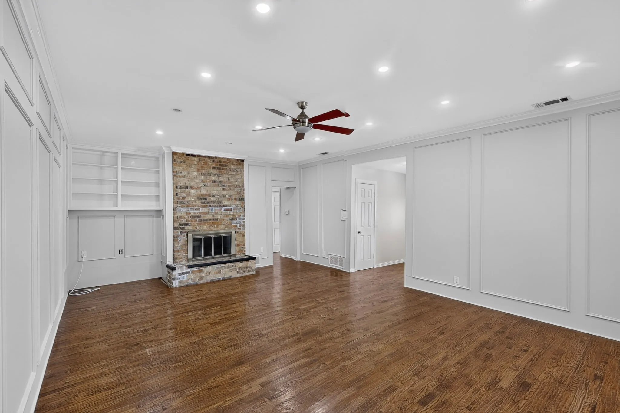 Wood flooring, recessed lighting, brick fireplace with a black hearth, built-in shelving, and decorative wall paneling
