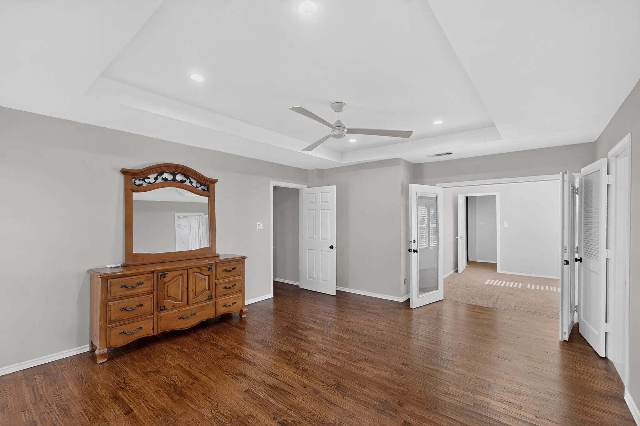 Wood-finish flooring, tray ceiling, recessed lighting, ceiling fan, and French doors