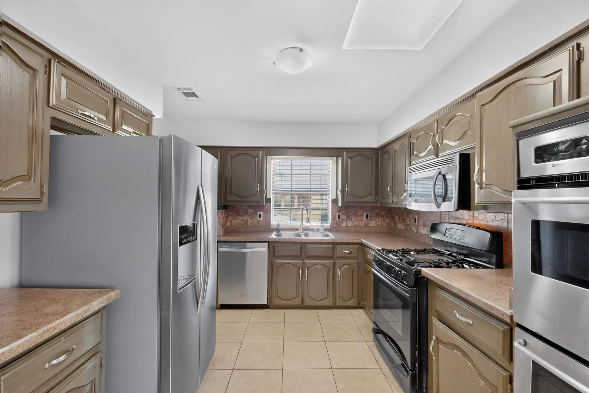 Kitchen featuring wood-finish cabinetry, tile flooring, stainless steel appliances, and a built-in microwave