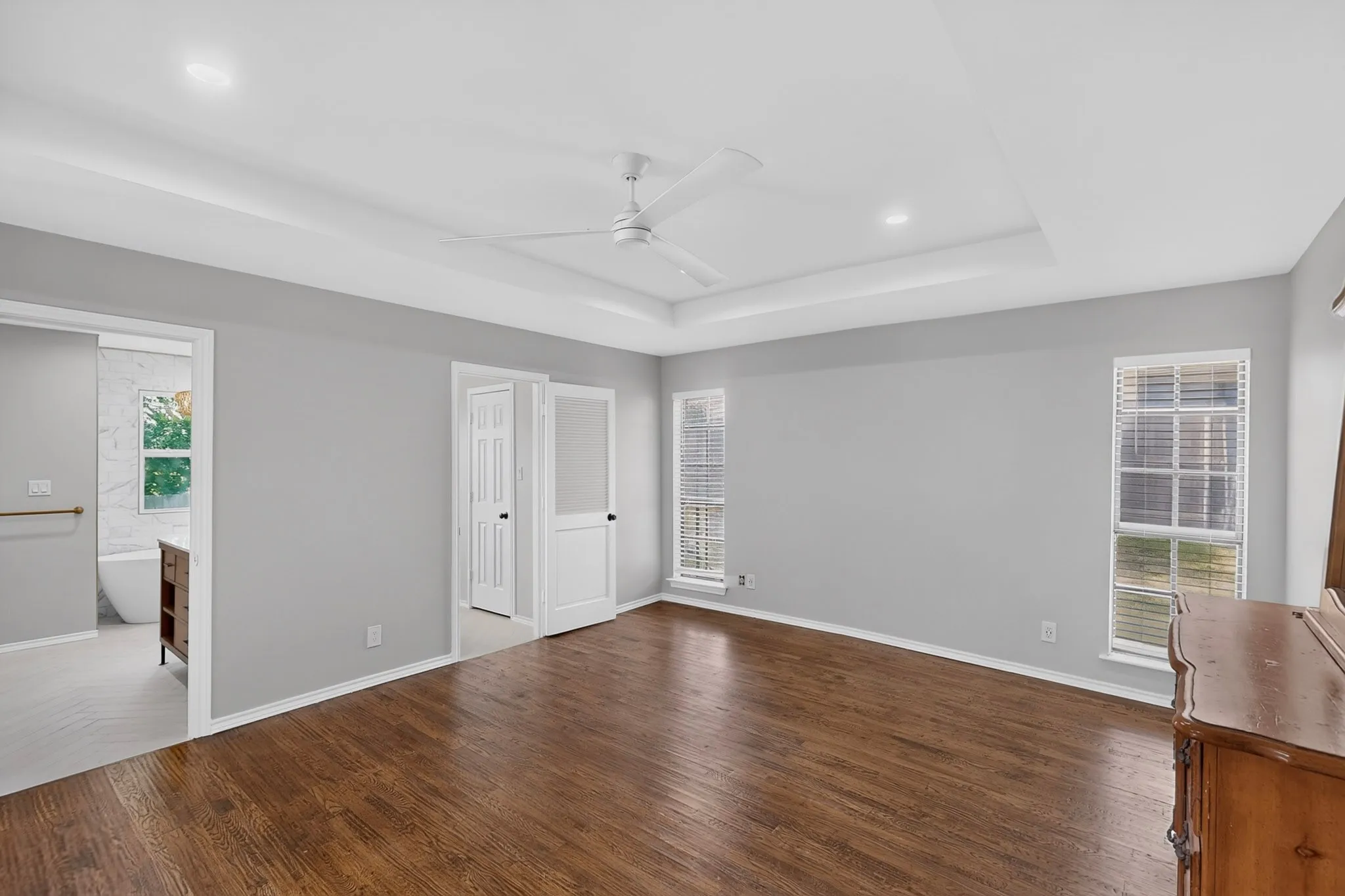 Tray ceiling with recessed lighting, wood-finish flooring, and white ceiling fan