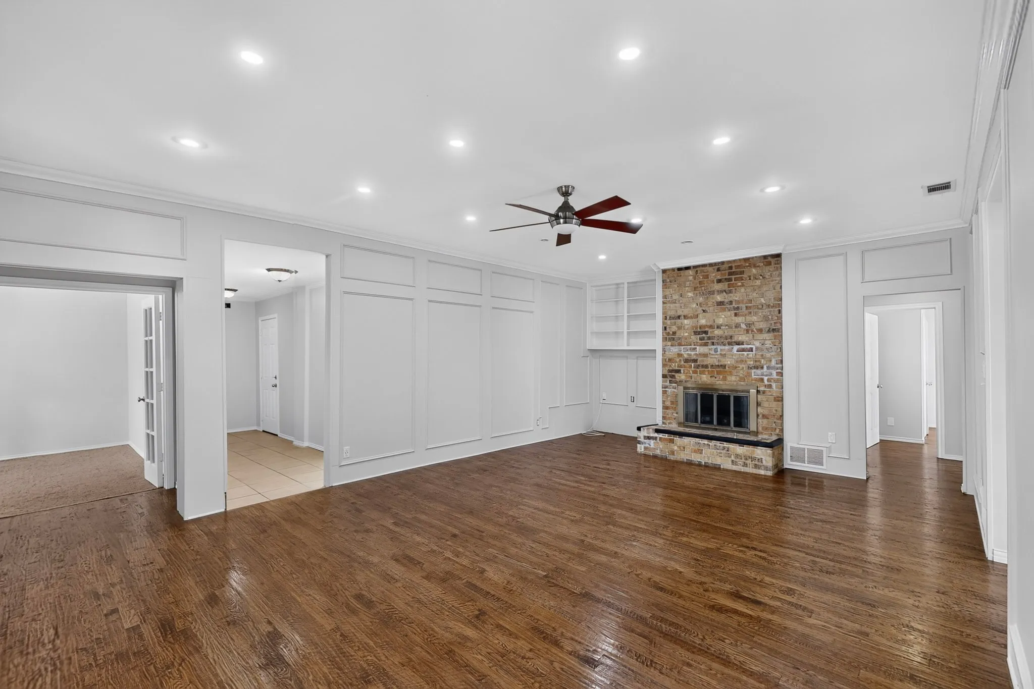 Hardwood flooring throughout, featuring a brick-face fireplace with hearth, built-in shelving, recessed ceiling lighting, and crown molding