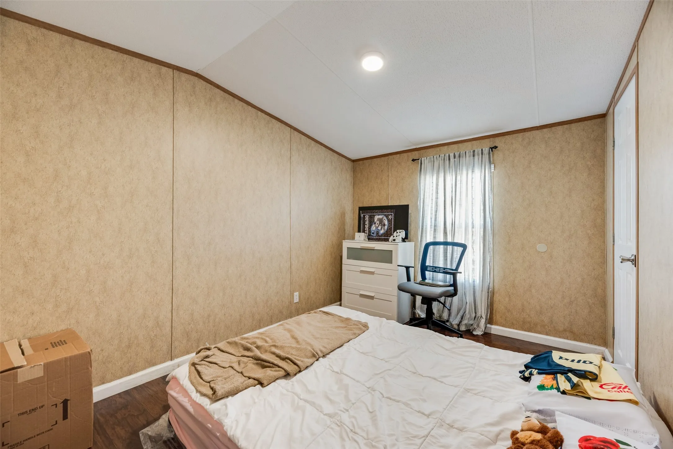 Wood-finish flooring, recessed ceiling lighting, light-toned wall paneling, and a window with curtain rod