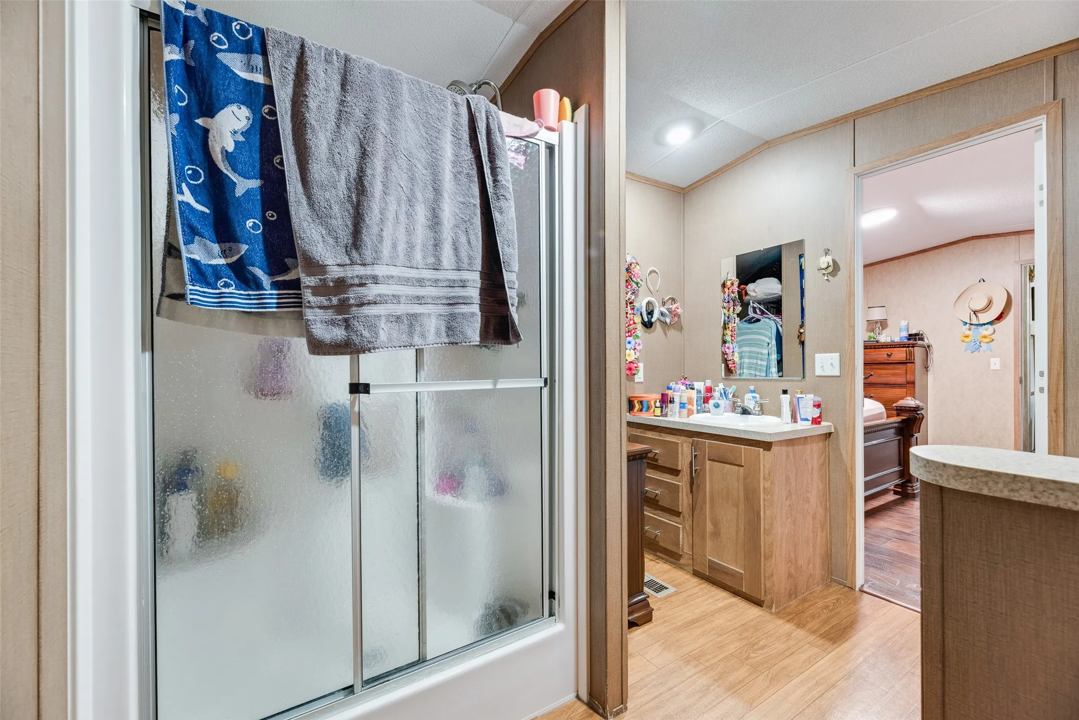 Enclosed shower, wood-finish flooring, vanity with integrated sink, wood-finish cabinetry, and wall-mounted mirror