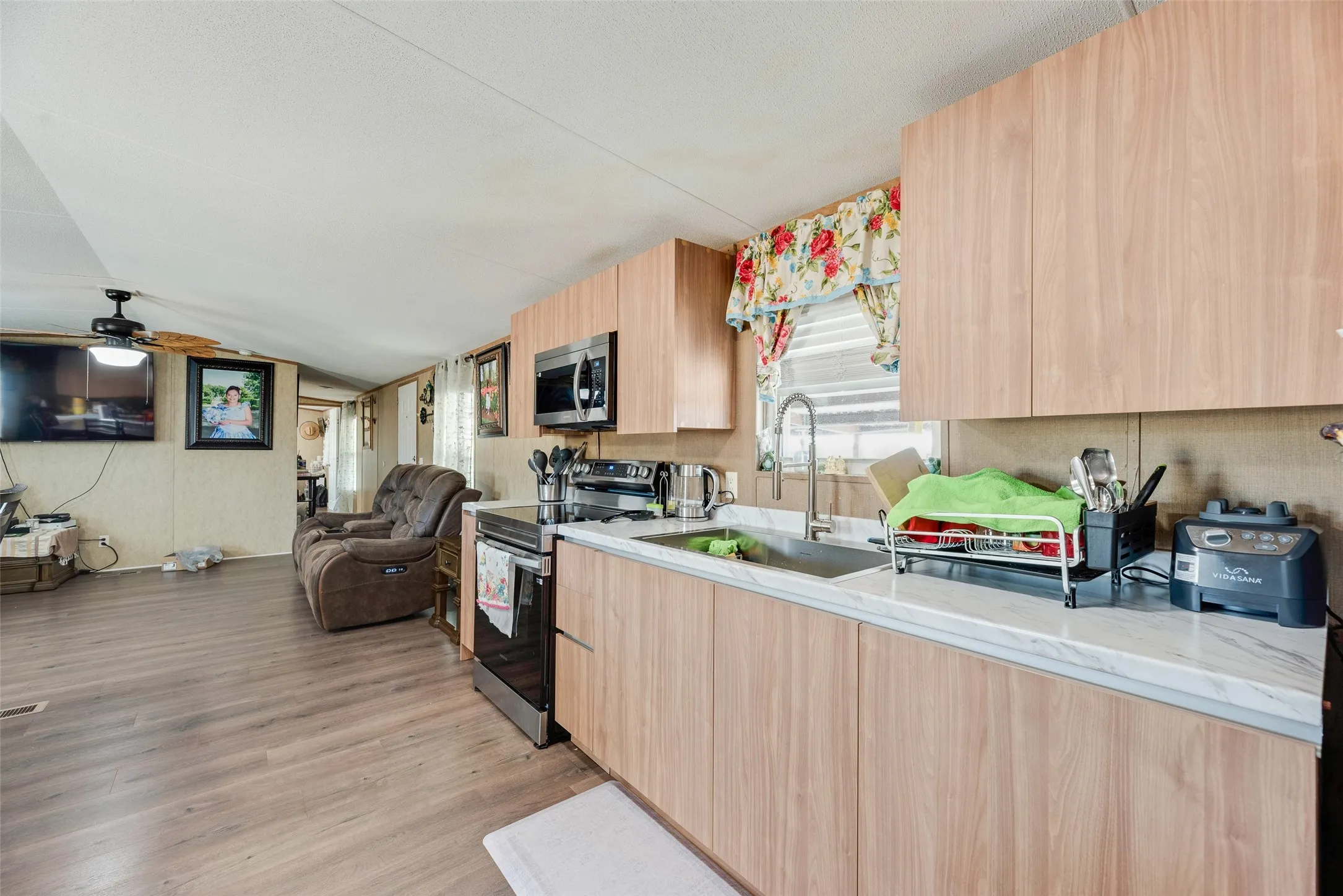 Kitchen featuring wood-finish cabinetry, stainless steel sink with gooseneck faucet, light-toned countertops, and integrated stainless steel microwave and range