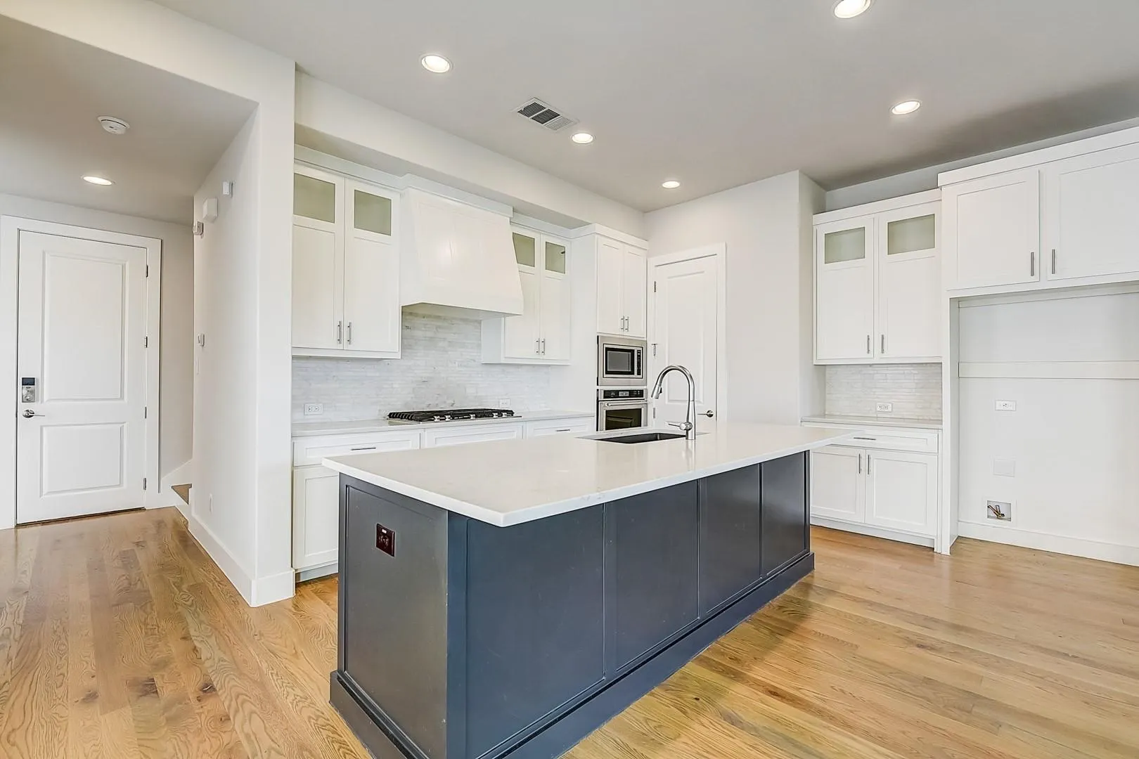 Spacious kitchen featuring an island with a white countertop, wood-finish flooring, white cabinetry, and recessed lighting