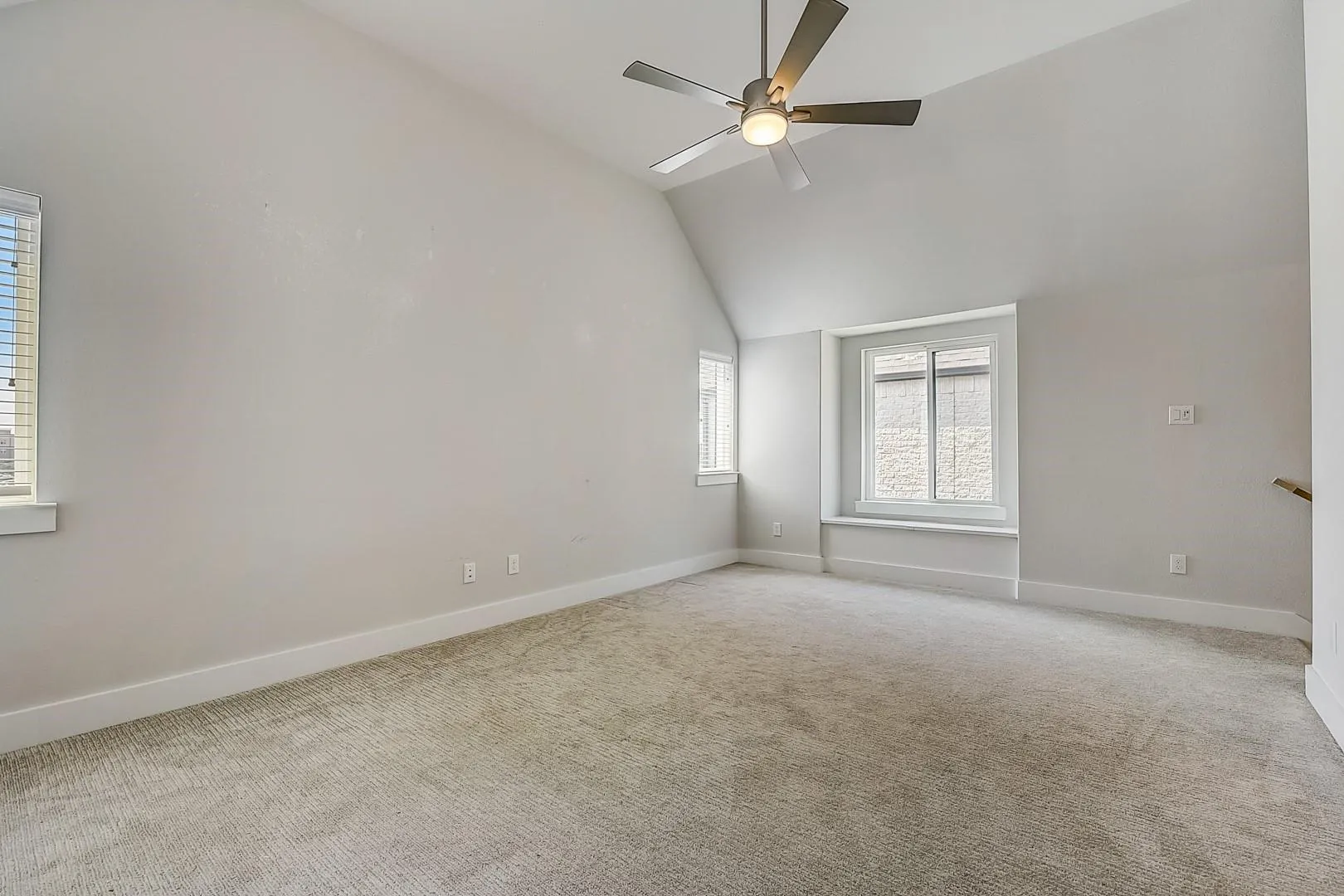 Vaulted ceiling with a ceiling fan, plush carpet flooring, multiple windows, and a window seat