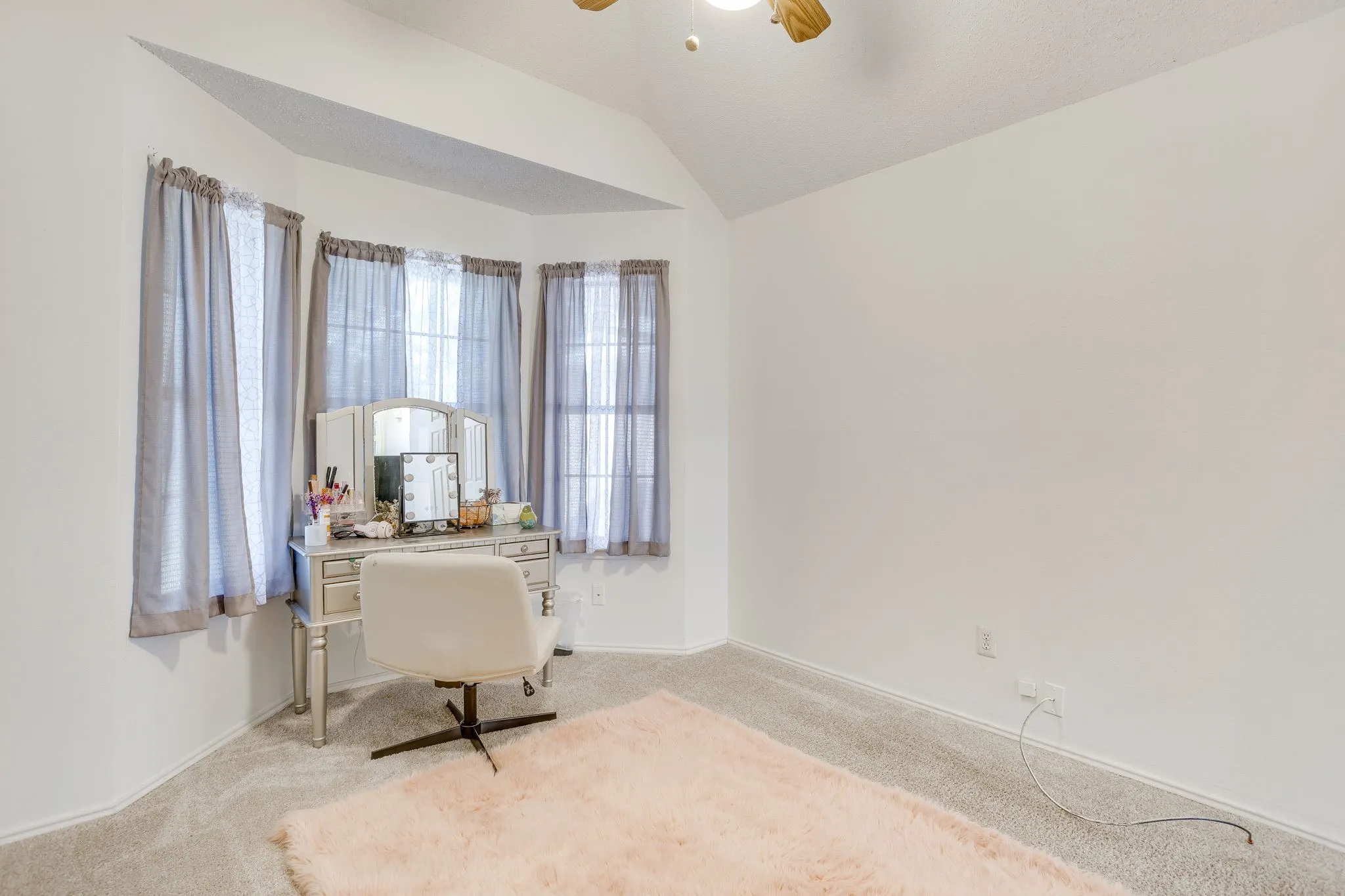 Bright corner bedroom with curved walls and vaulted ceiling, featuring multiple windows with sheer curtains providing abundant natural light