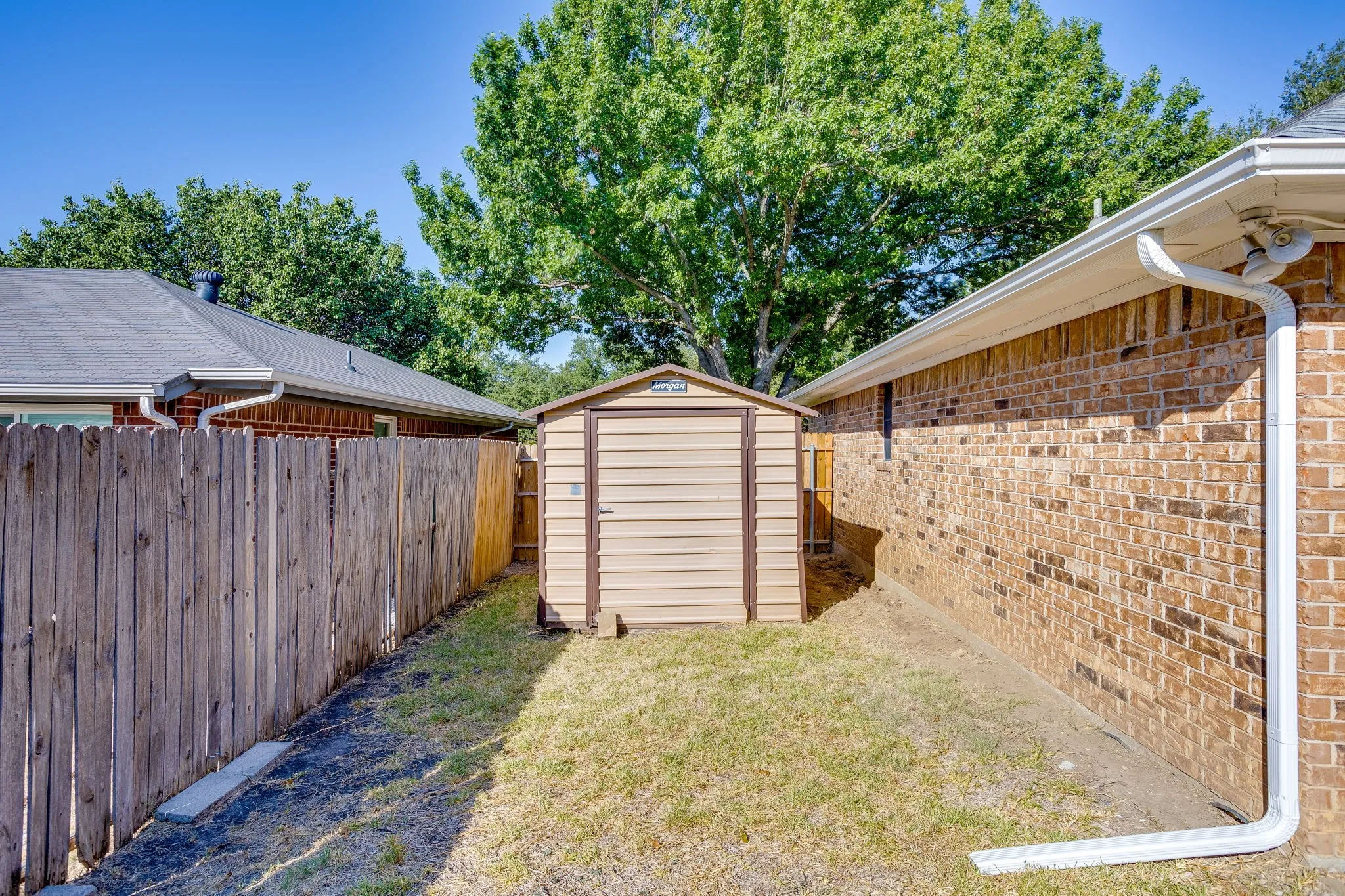 Outdoor storage shed with vertical paneling, wood privacy fencing, and a brick exterior wall