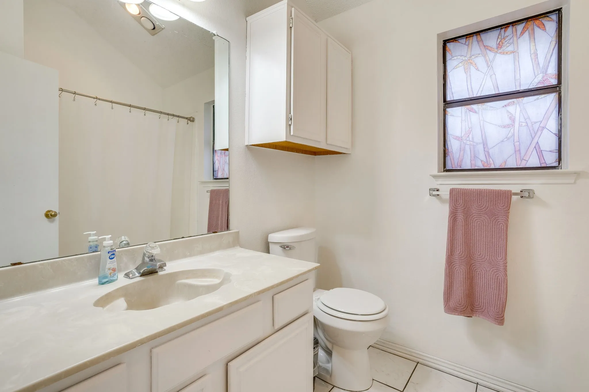 Bathroom featuring a vanity with integrated sink, white cabinetry, tiled flooring, a window, and a built-in toilet