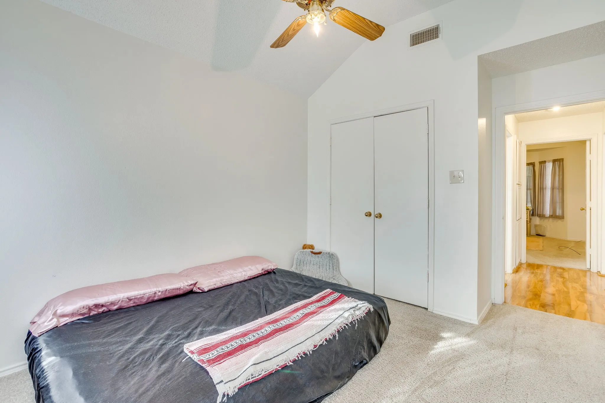 Spacious bedroom #3 with vaulted ceiling and ceiling fan, white double closet doors, and warm wood-finish flooring throughout