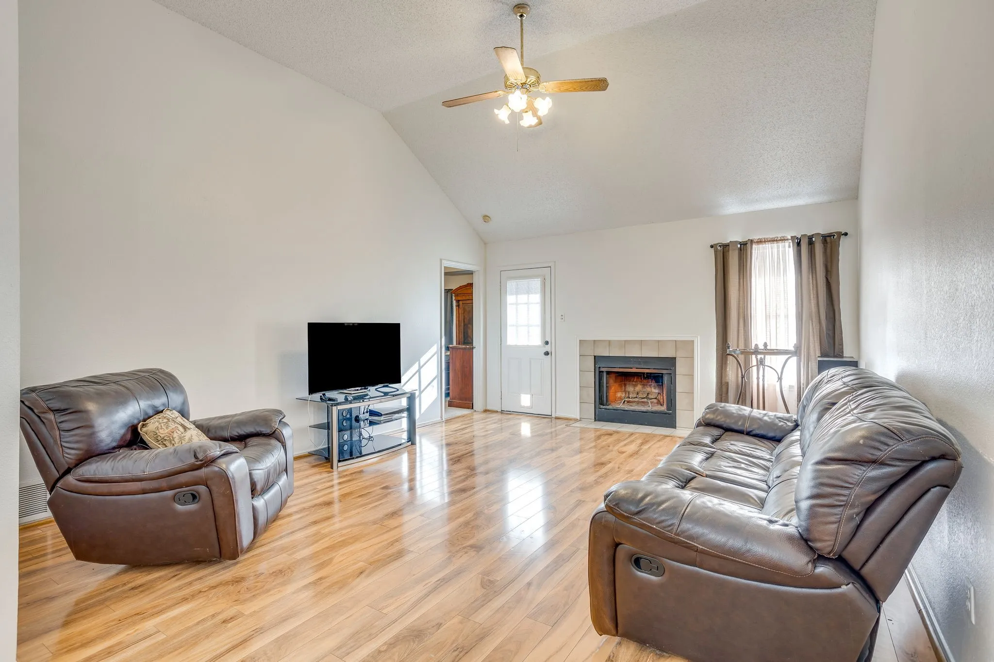 Vaulted ceilings with a ceiling fan, wood-finish flooring, and a fireplace with a tile surround
