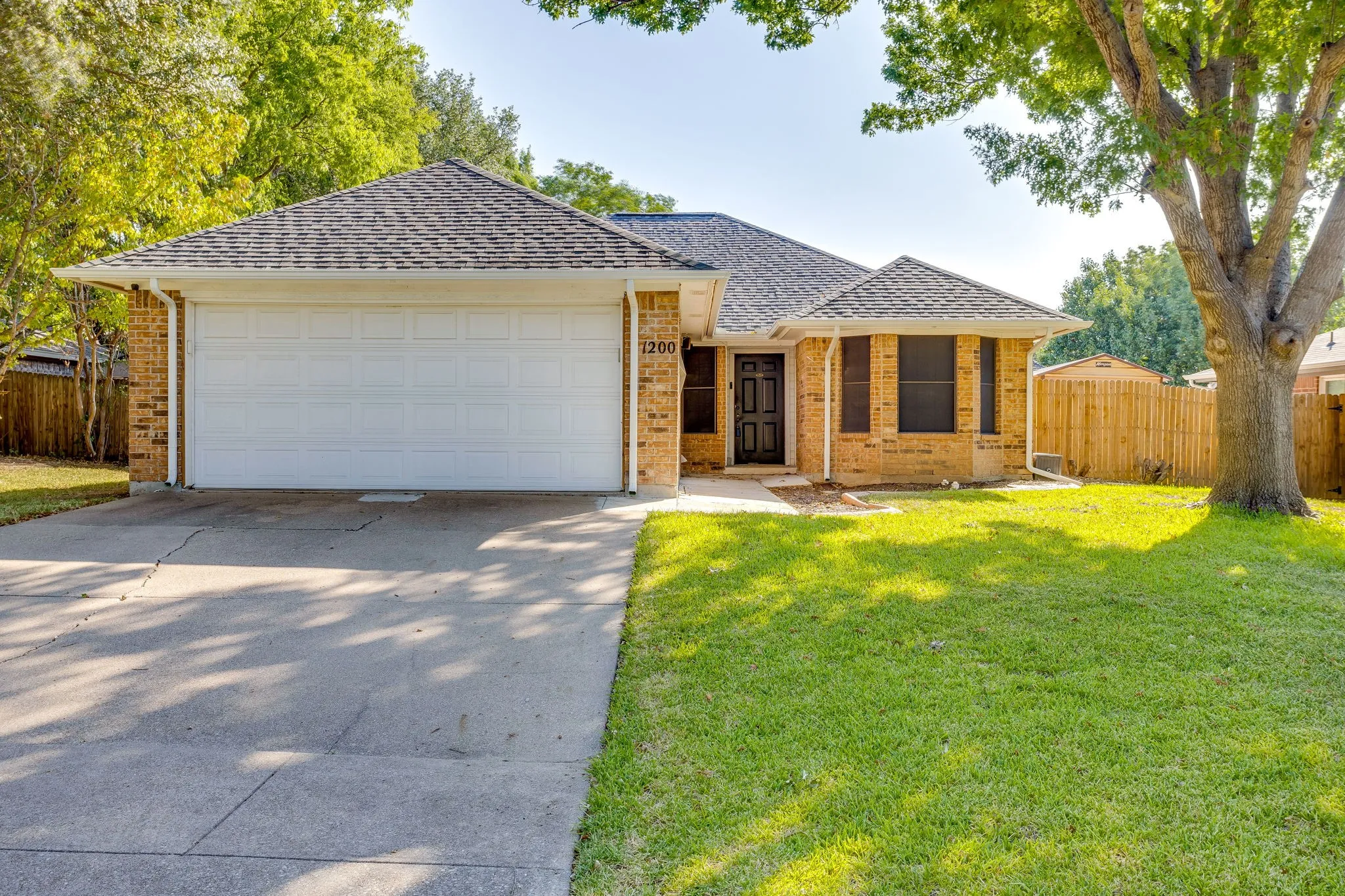 Brick exterior with an attached two-car garage, concrete driveway, and a mature tree