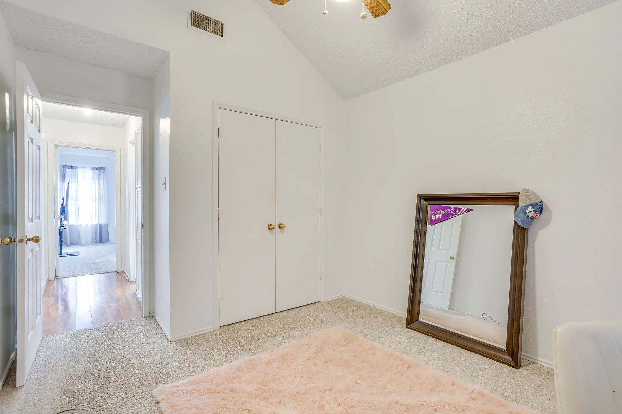 Bedroom #2 with vaulted ceiling, ceiling fan, white bi-fold closet doors, brass hardware, and carpet flooring